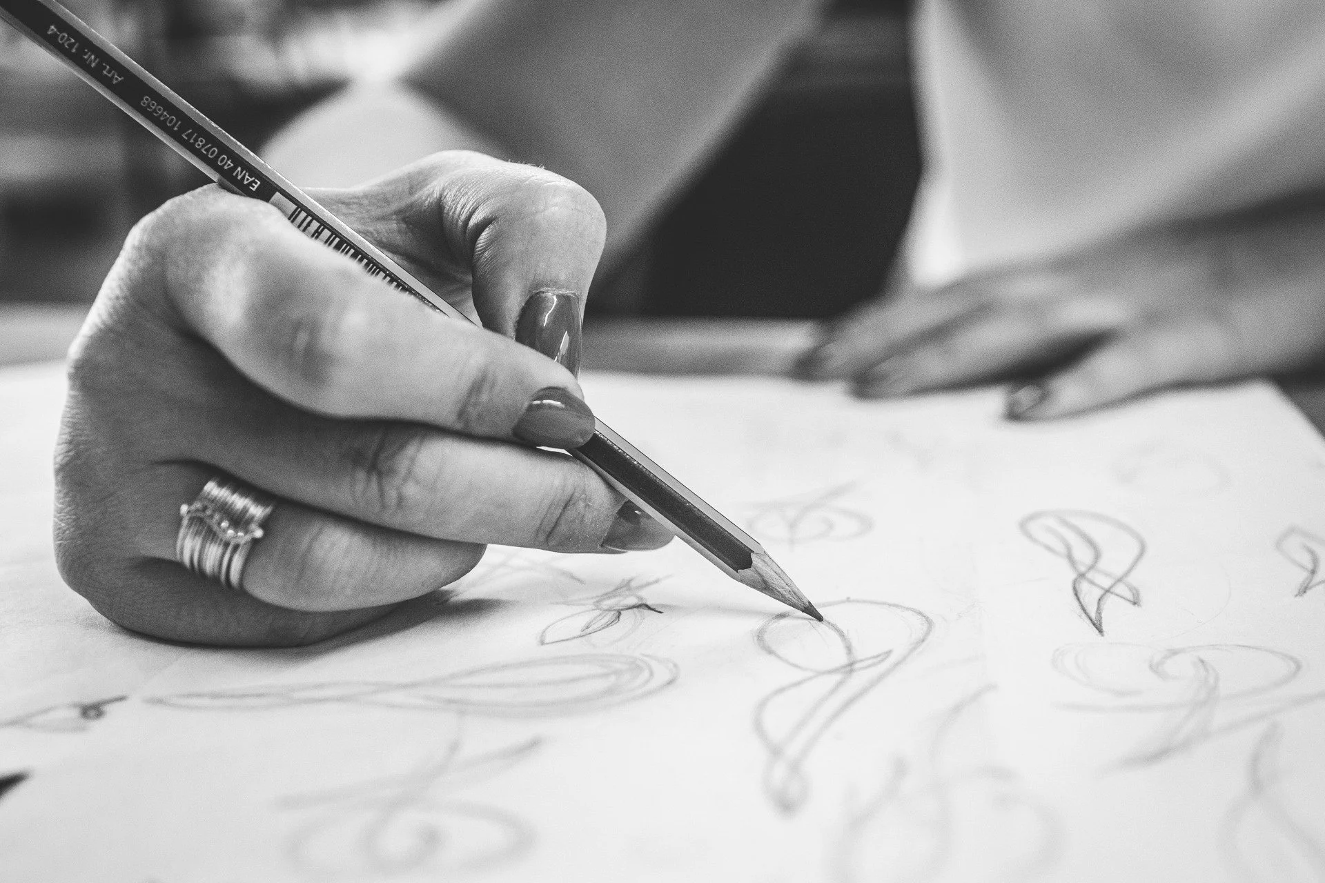 Mão de uma pessoa desenhando com lápis em papel, com foco na mão e no lápis em preto e branco.