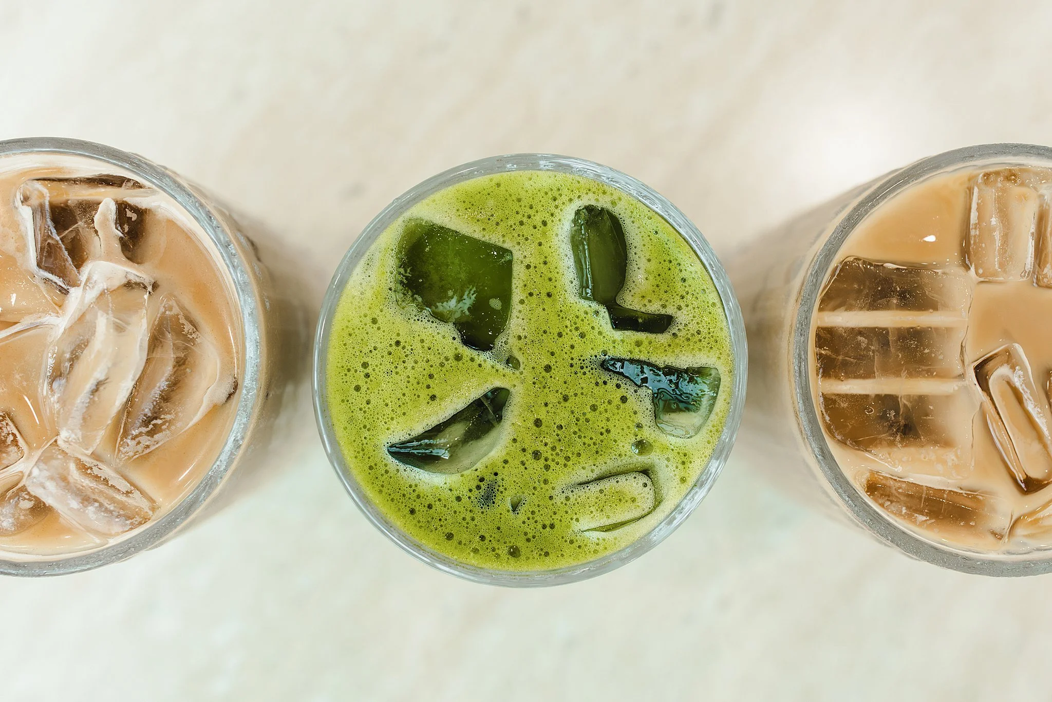 Three glasses of iced drinks on a white surface, with the middle one filled with green matcha and ice cubes, and the other two with coffee and ice cubes for branding session near me.