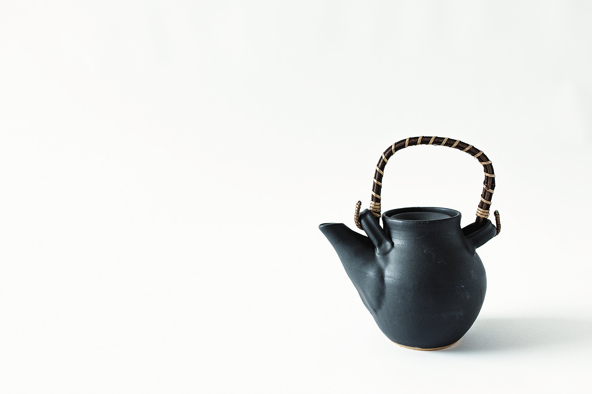 Black teapot with a woven handle on a plain white background for product photography by Ally and B Photography.