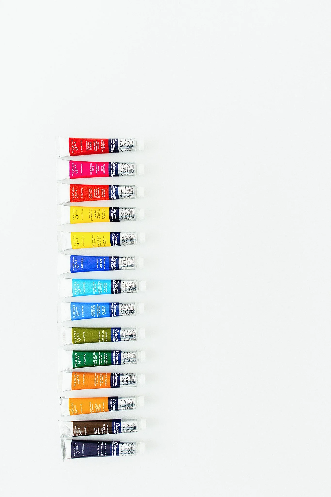 A vertical row of 12 paint tubes in various colors on a white background during an artist branding photography session.