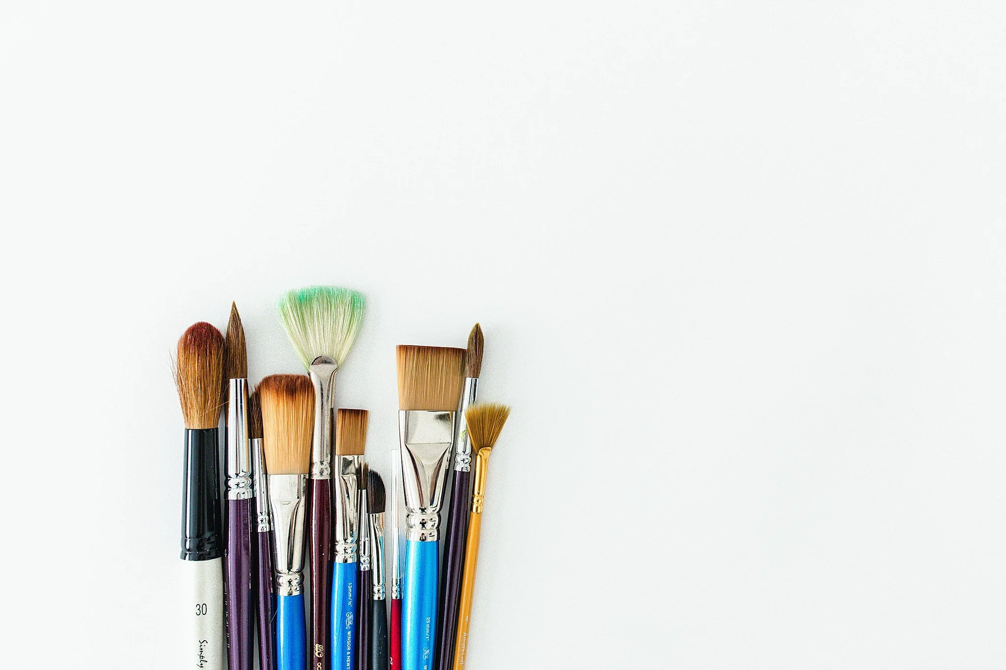 A collection of various paintbrushes with colorful bristles arranged on a white background for product photography in Naperville, IL.
