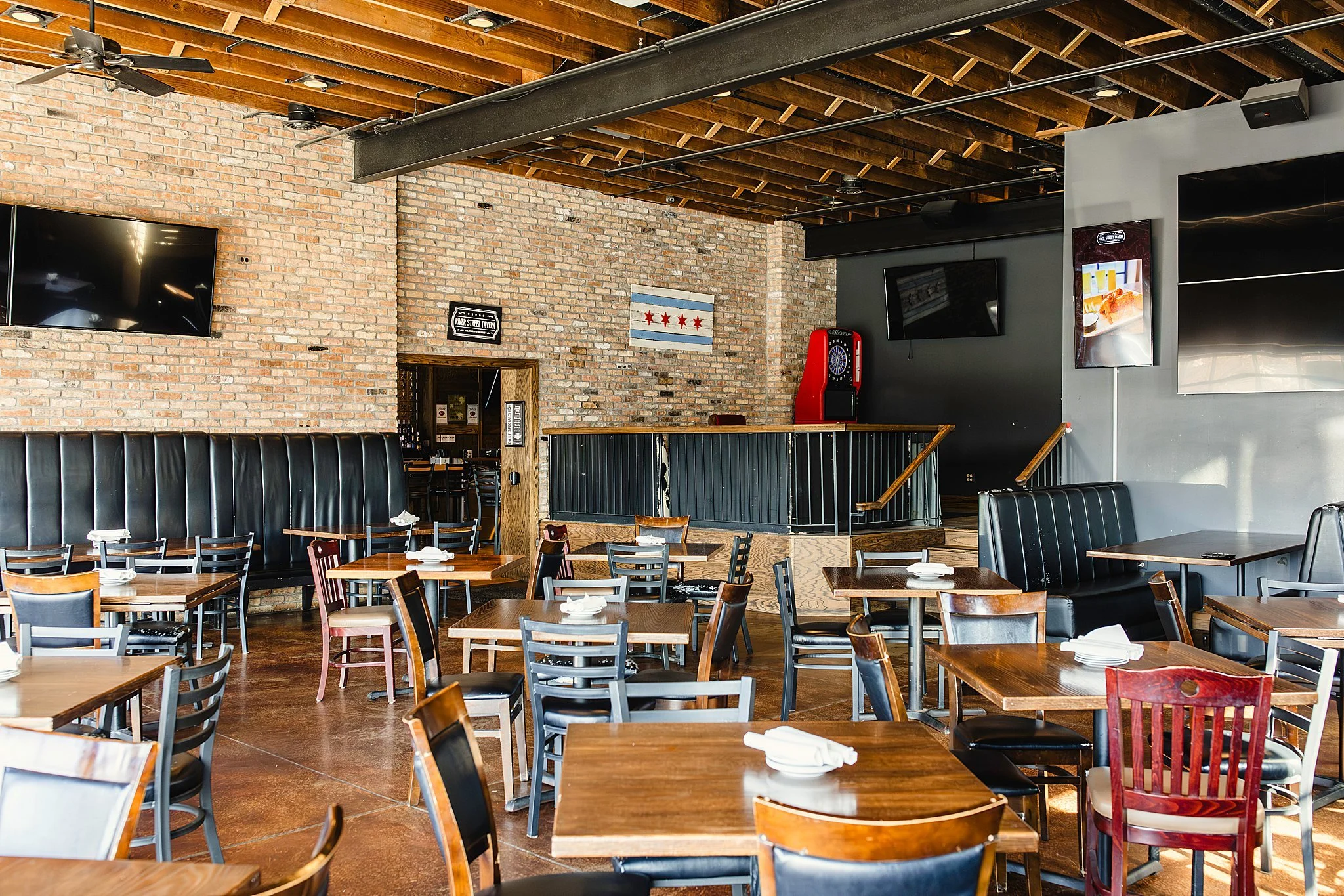 Interior of a restaurant with wooden tables and chairs, exposed brick walls, and a ceiling with exposed wooden beams and black metal piping for food and drink branding photographers near me.