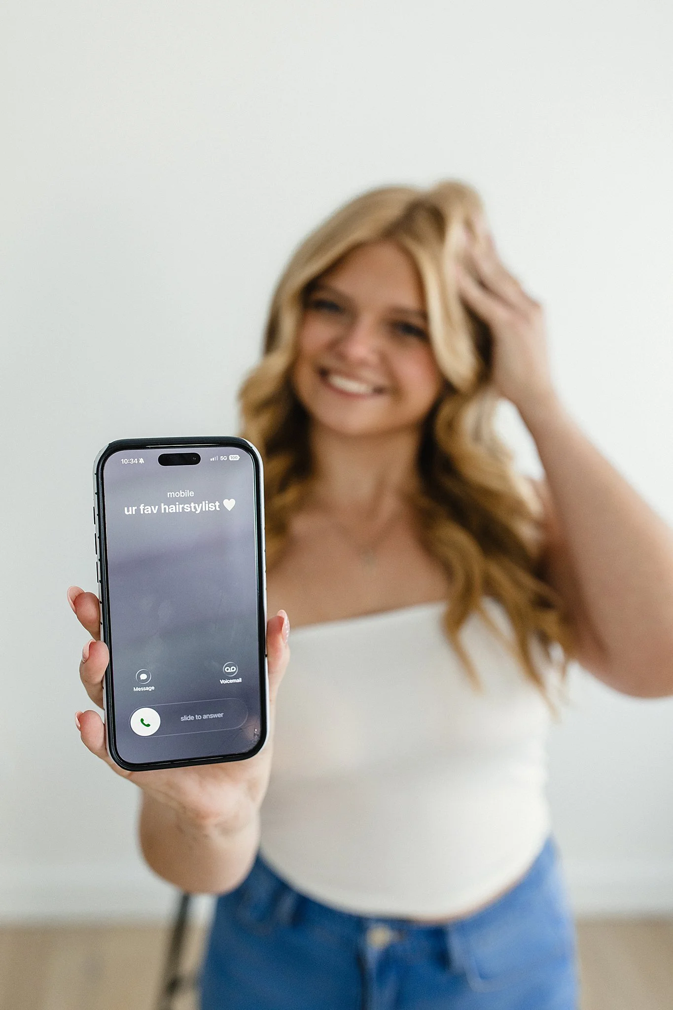 A woman holding a smartphone with a missed call notification from a hair stylist, smiling in the background for a hairstylist branding photoshoot with Ally and B Photography.