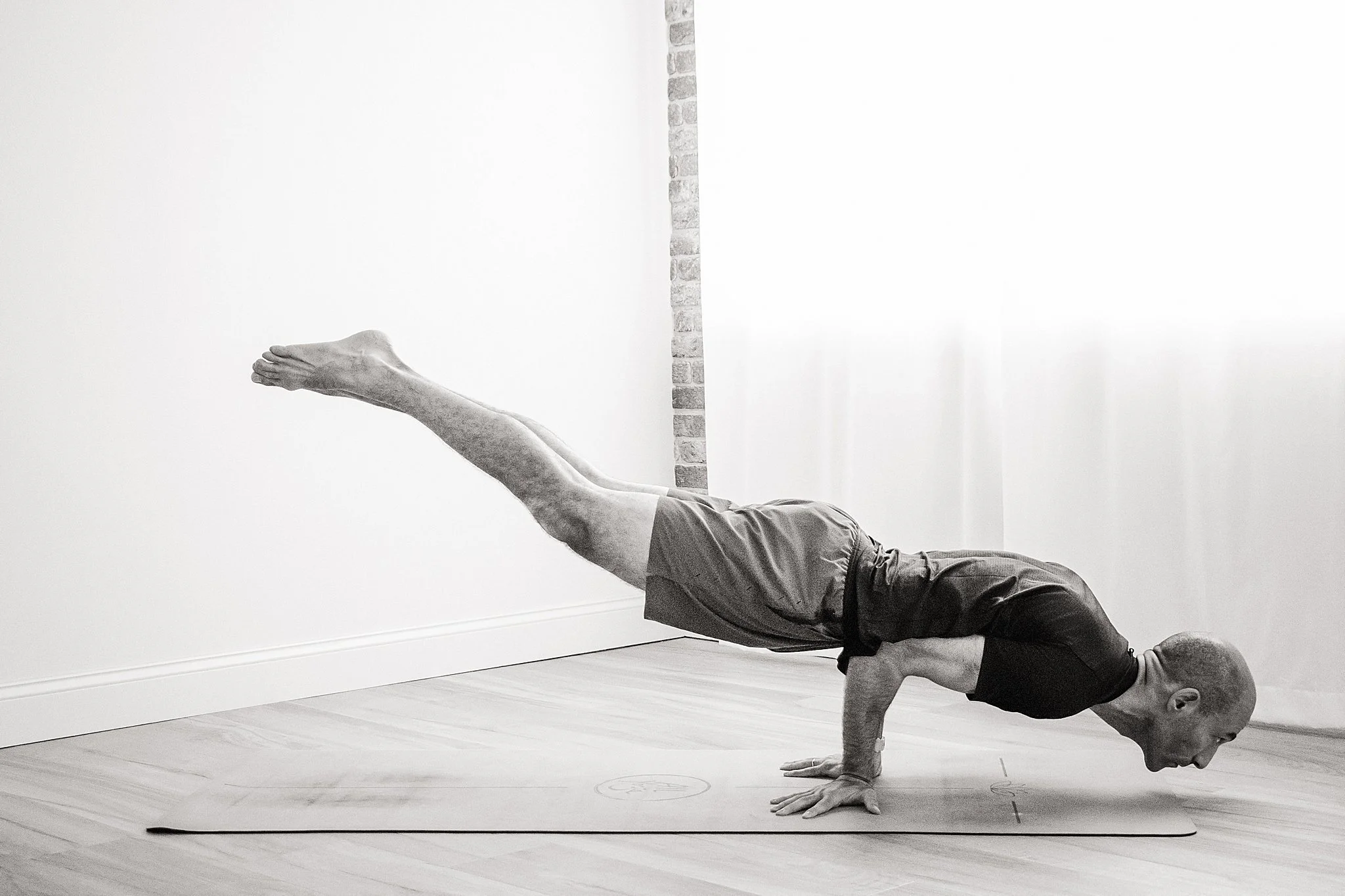 A man in athletic clothing performing a yoga pose balancing on his hands with legs extended upwards in an indoor space during a yoga branding session in Naperville, IL.