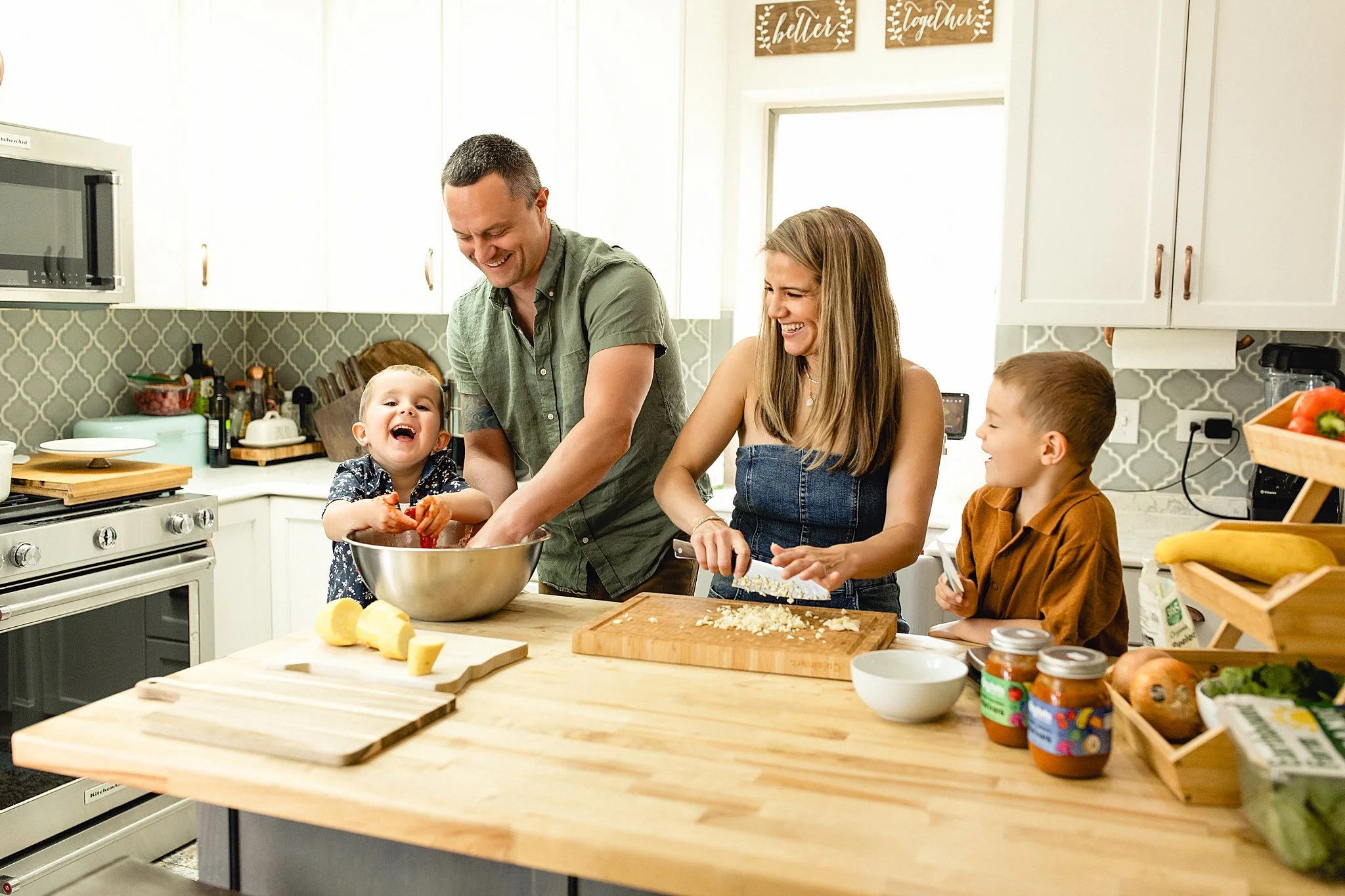 Family of four in a kitchen preparing food together, cooking and laughing during a brand photoshoot with Ally and B Photography in Naperville, IL.