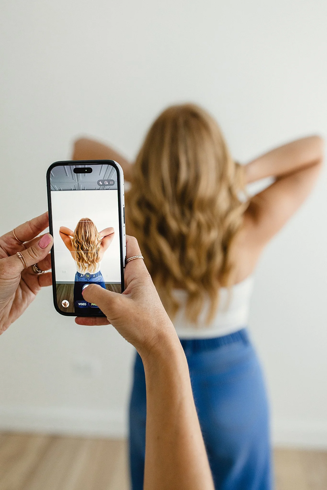 Person taking a photo of a woman with long, wavy red hair from behind using a smartphone with branding photographers near me.