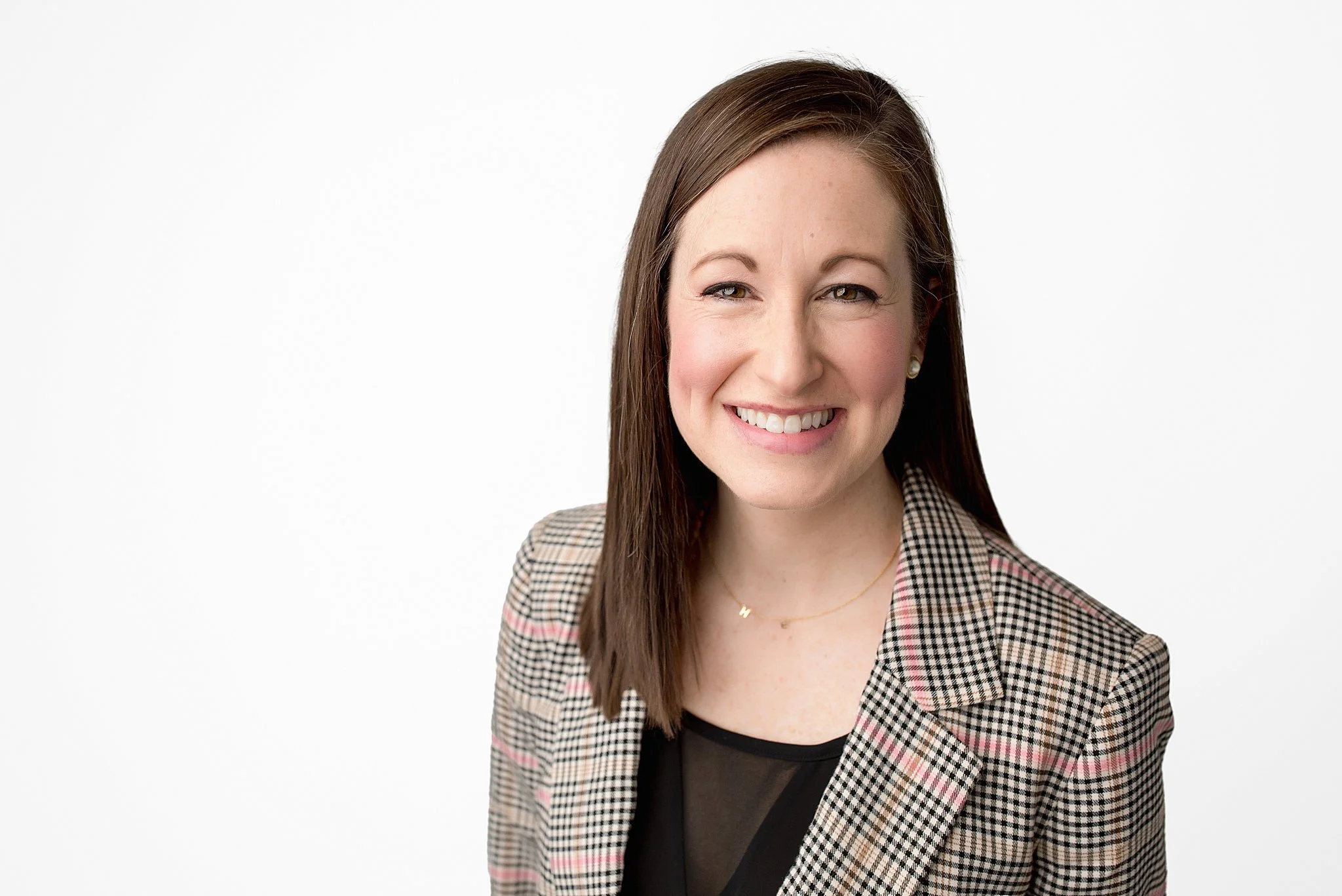 Portrait of a smiling woman with straight brown hair, wearing a checkered blazer and black top against a white background during Naperville headshots.
