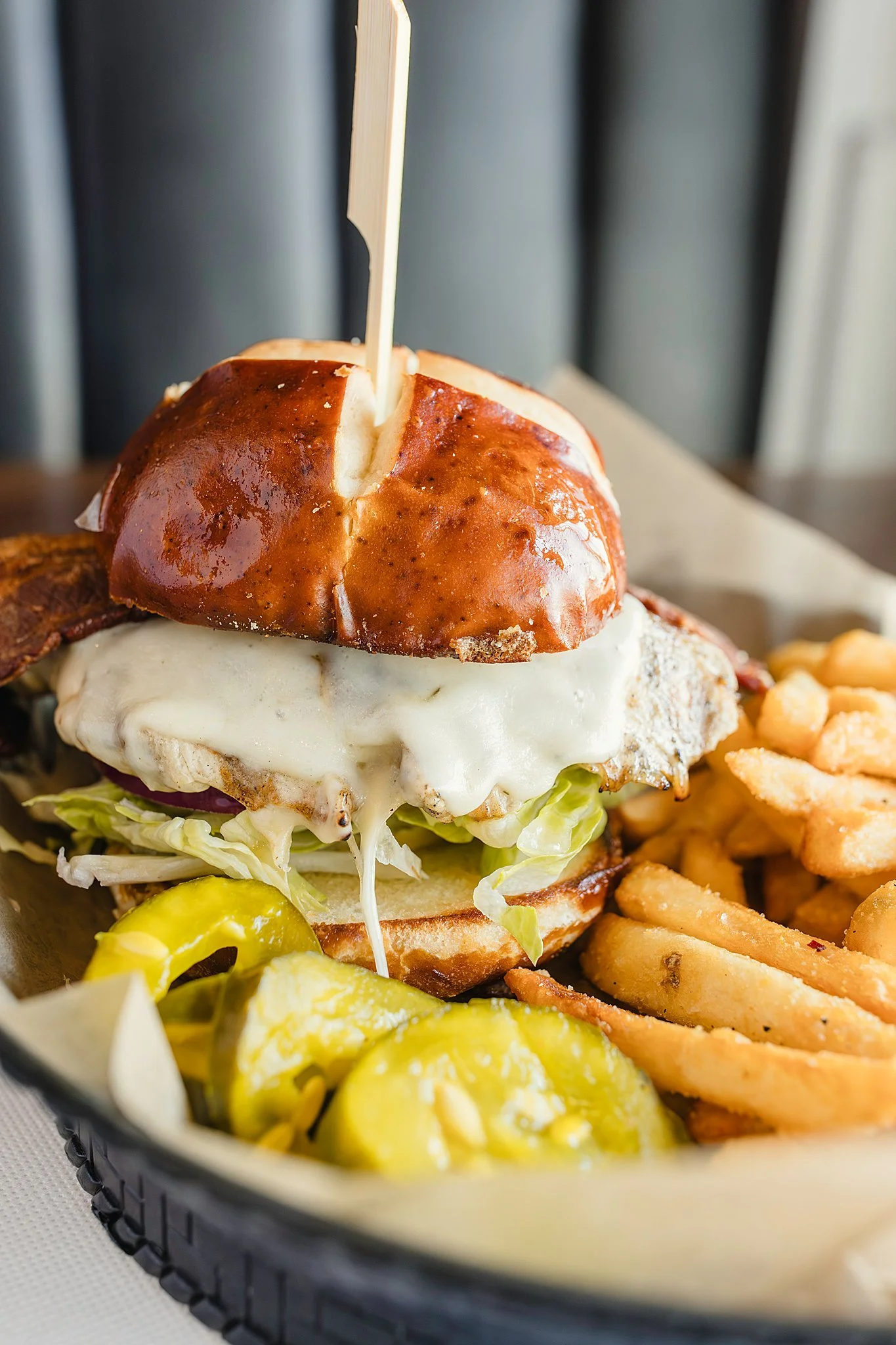 Close-up of a gourmet bacon cheeseburger with fried egg, lettuce, and pickles, served with French fries on the side during a bar and restaurant branding photography session for food photography of menu items.