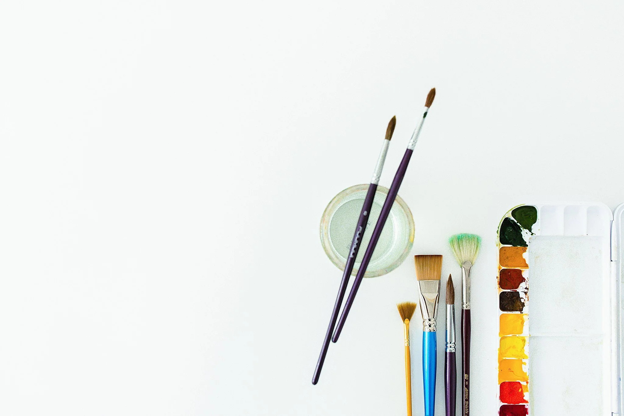 Assorted watercolor paints and brushes on a white surface for art product photography near me.