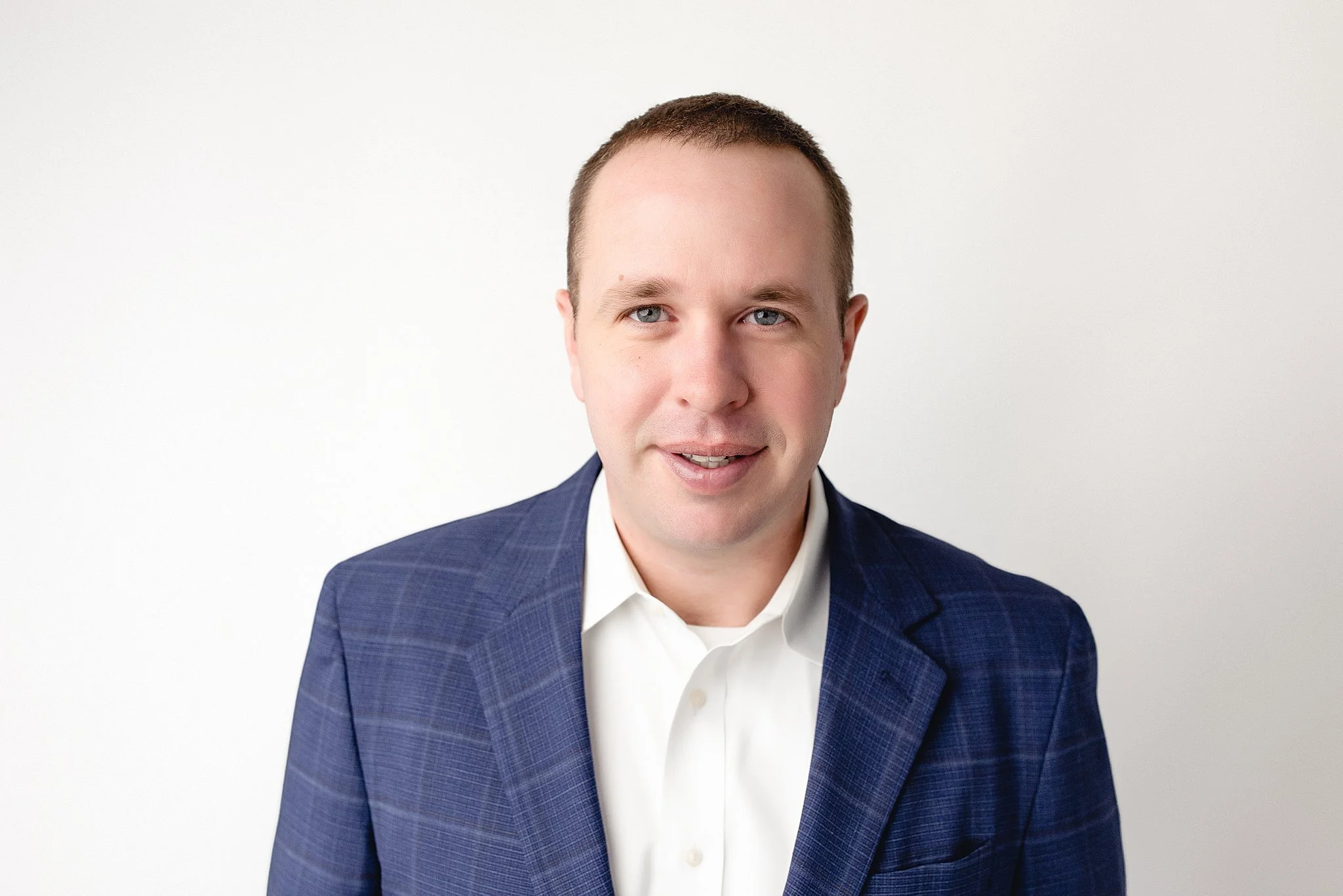 Portrait of a man with short brown hair, blue eyes, wearing a white shirt and a navy blue blazer, against a plain white background during a headshot photo session in Naperville, IL.