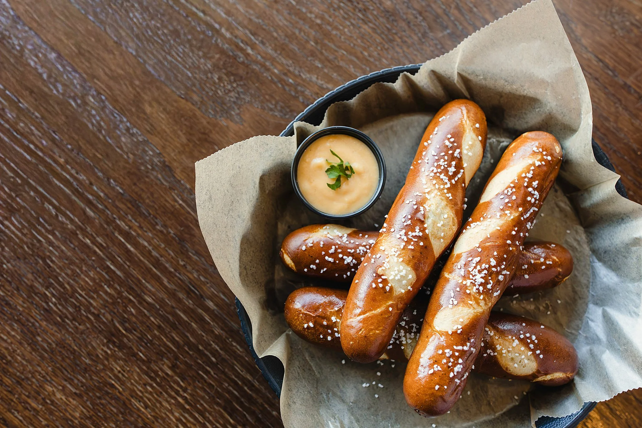 Pretzel sticks topped with coarse salt served with a dipping sauce garnished with a small herb leaf during a restaurant brand photography session for food photography of menu items.