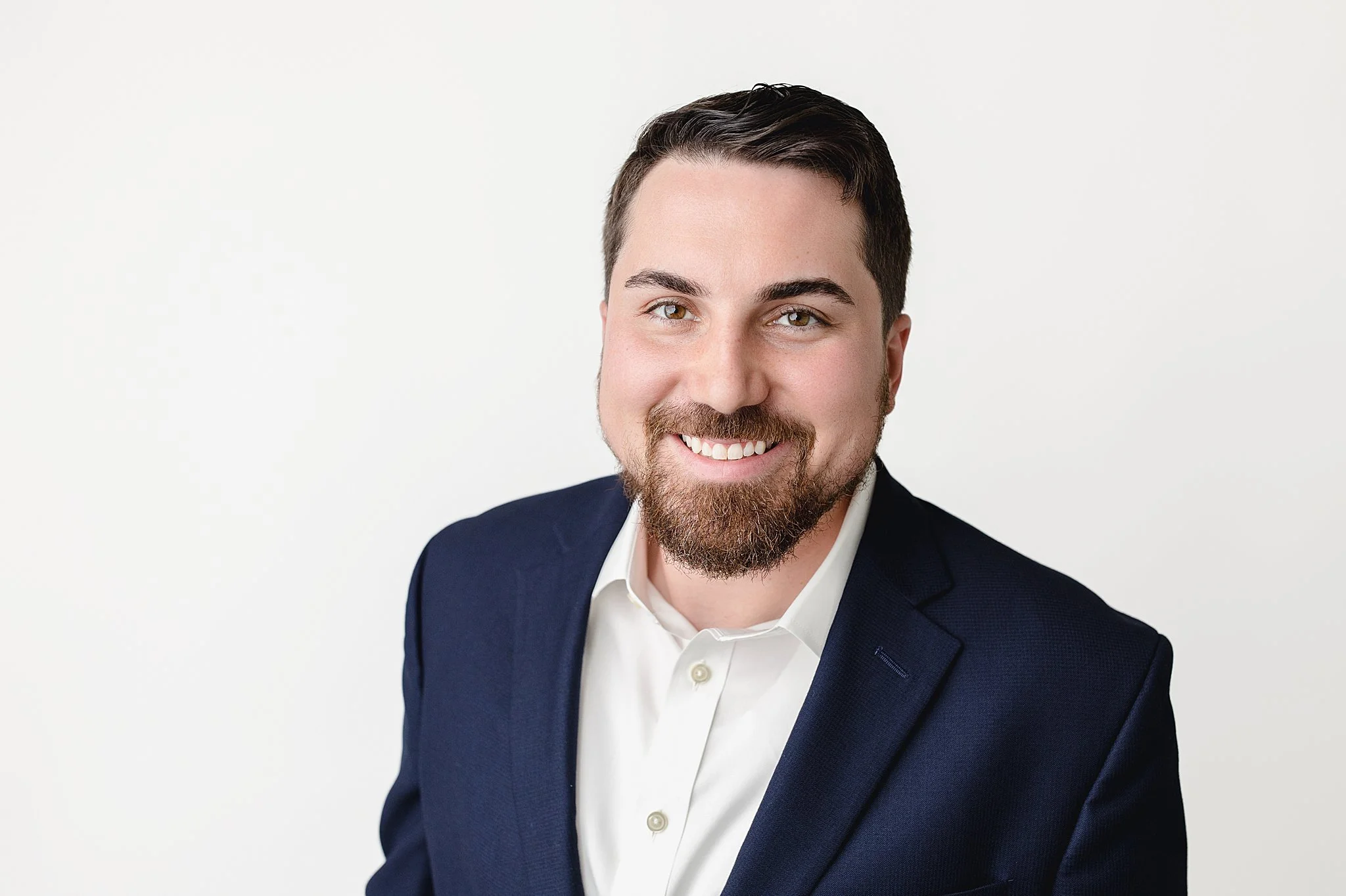 Headshot of a smiling man wearing a navy blazer and white shirt against a plain white background for headshots with Ally and B Photography in Naperville, Illinois.