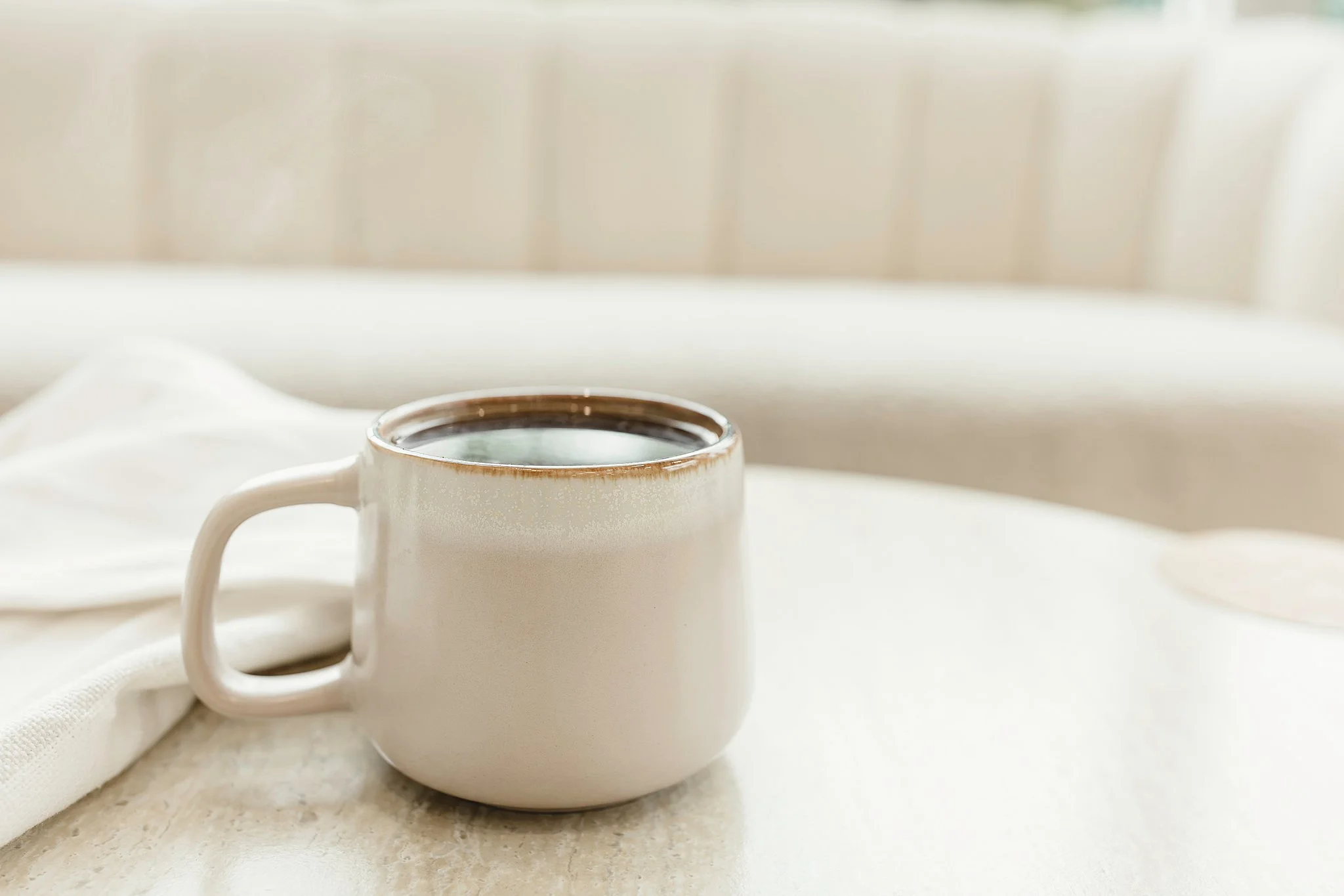 Close-up of a white coffee mug filled with a dark beverage, placed on a beige surface with a white cloth beside it for strategic brand imagery near me.