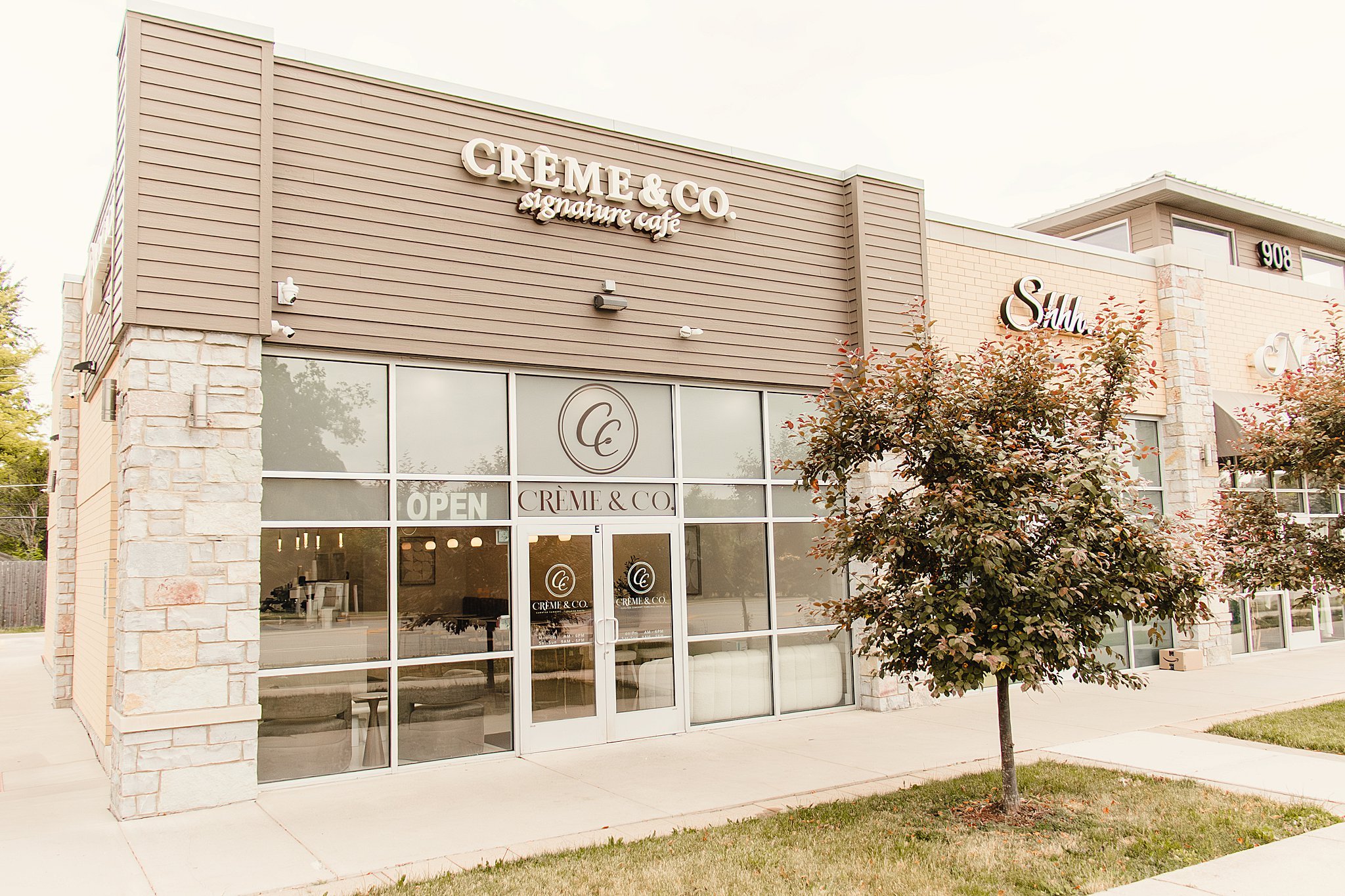 Exterior of a retail storefront with large windows, beige siding, stone accents, and signage reading Creme & Co. signature cafe. A small tree with reddish leaves is in front of the store with branding photographers Naperville.