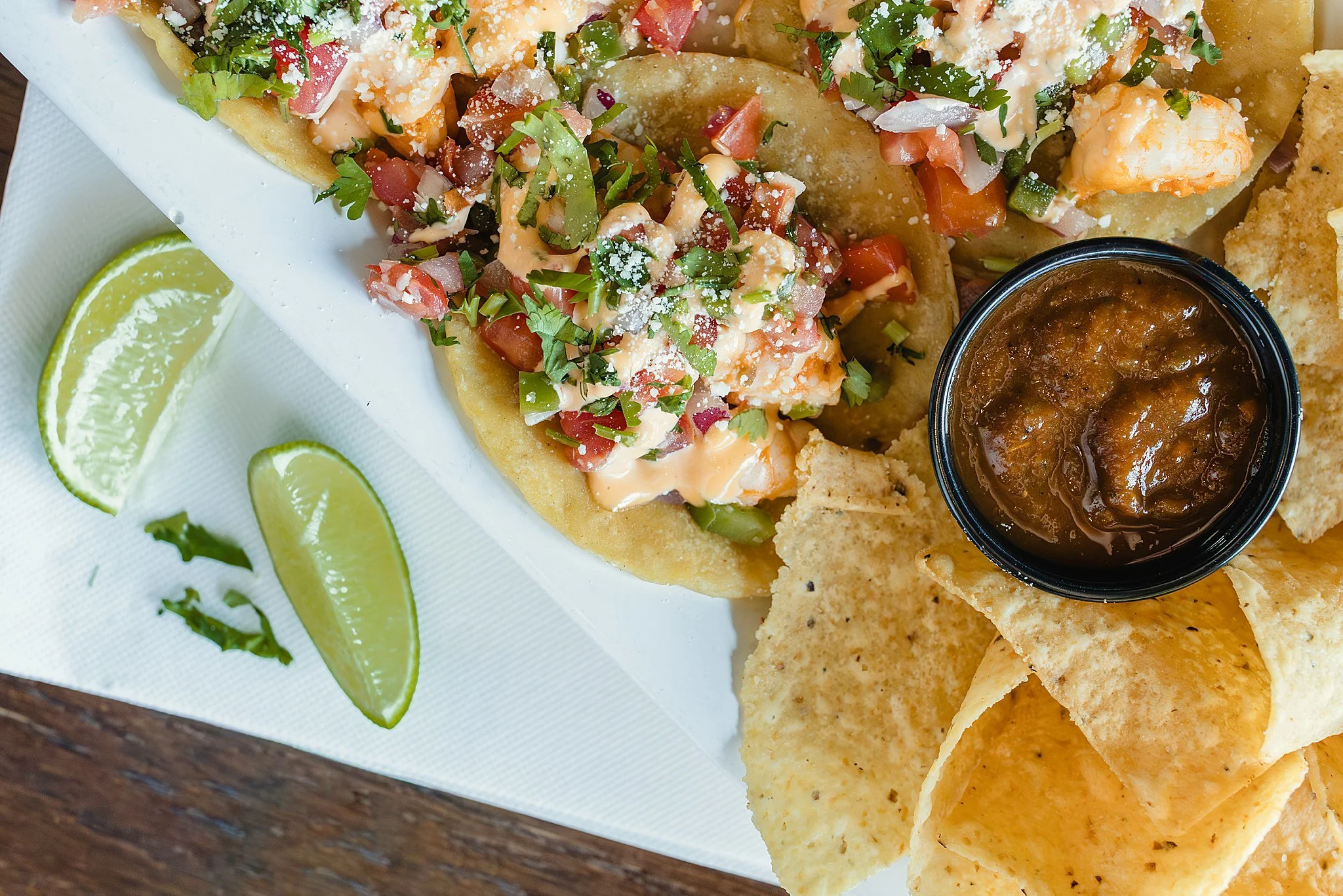Tacos with chopped tomatoes, cilantro, sauce, and shredded cheese, served with lime wedges, tortilla chips, and salsa with food photographers near Naperville, IL.