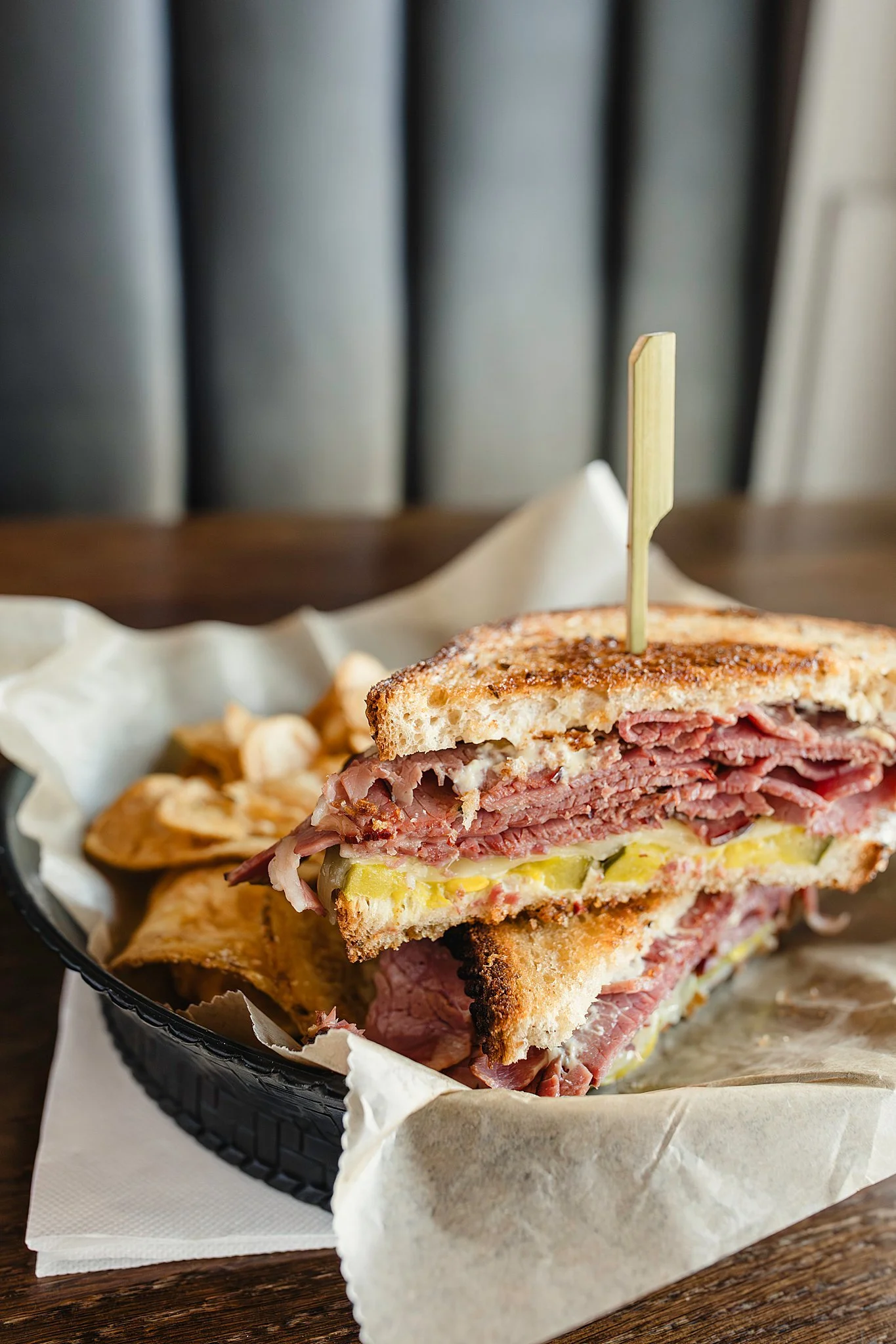 Close-up of a grilled reuben sandwich with corned beef, sauerkraut, Swiss cheese, and rye bread, served with potato chips during a commercial food photography session with Ally and B Photography.