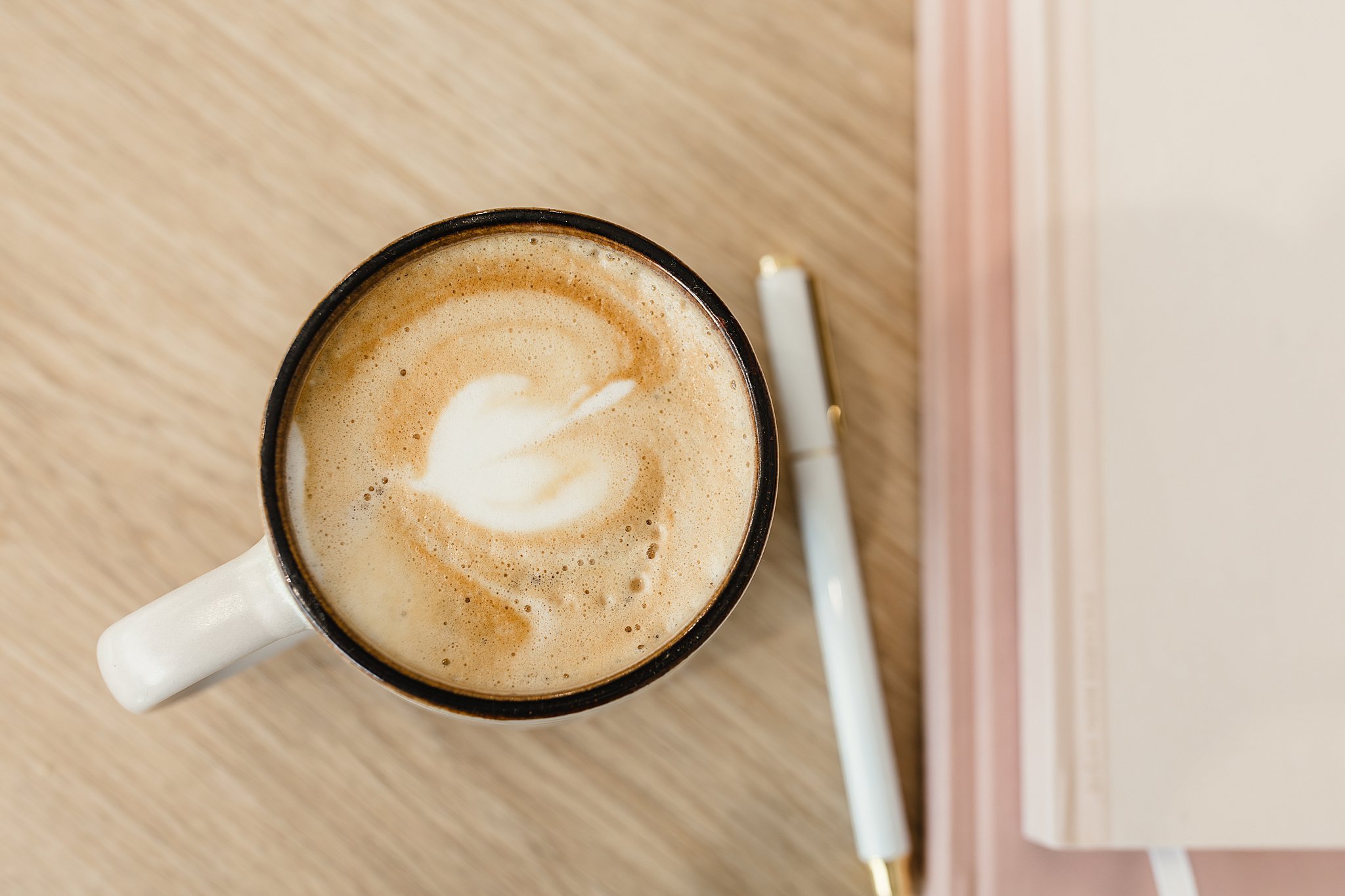 Top view of a coffee mug filled with a frothy beverage, possibly a latte, sitting on a wooden surface with a pen nearby with Naperville brand photographer.