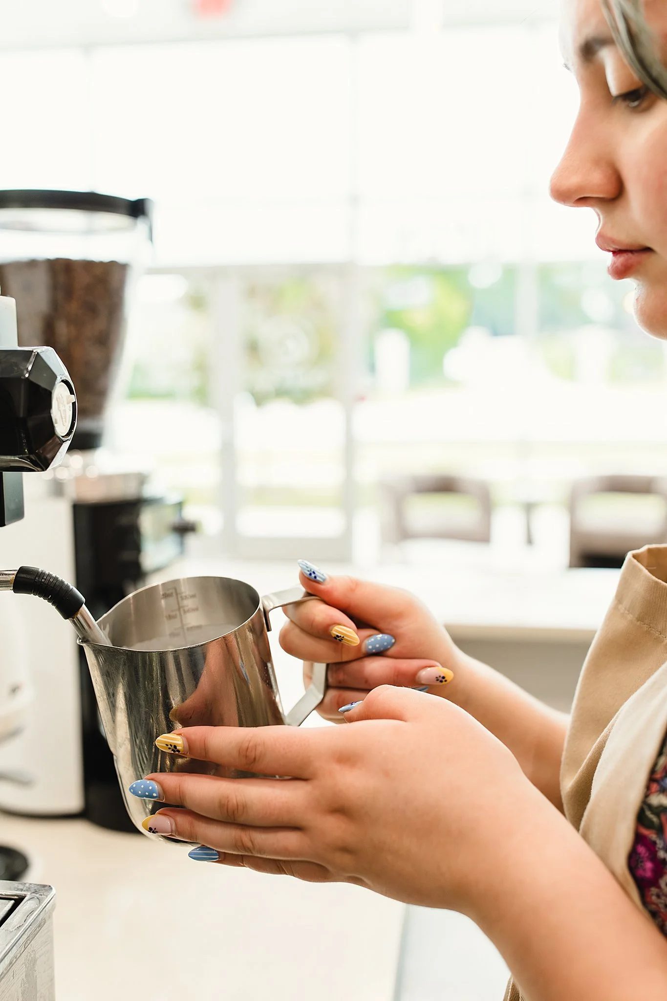 A person with painted nails pouring a liquid from a metal container into a coffee machine for branding photography with Marie Lopez in Naperville, IL.