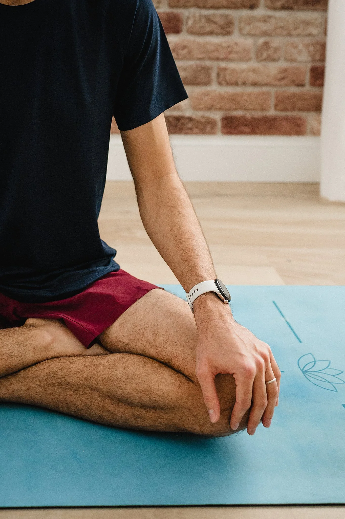 A person sitting cross-legged on a blue yoga mat with a lotus flower and line design, in front of a brick wall during a yoga branding photoshoot in Naperville, IL.