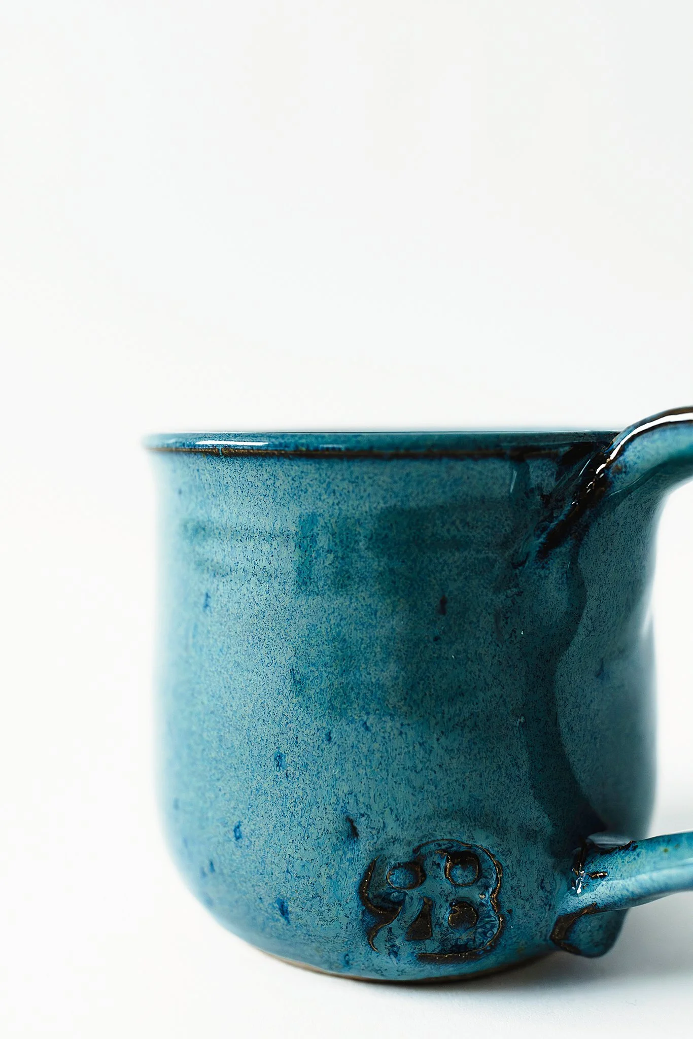 Close-up of a textured blue ceramic mug with a small emblem or marking near the handle against a plain white background for product photos near Naperville.