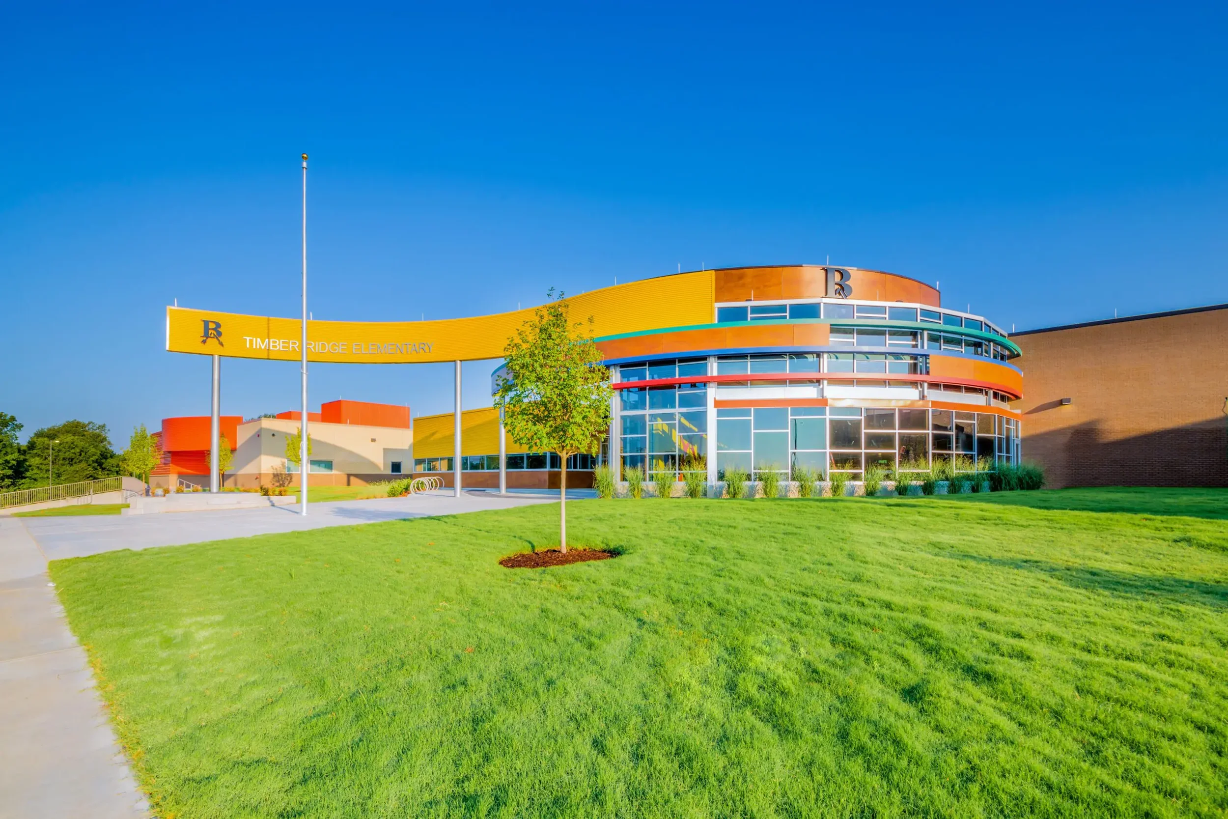 Exterior view of Timber Ridge Elementary School with a modern, colorful building, green lawn, and a clear blue sky.