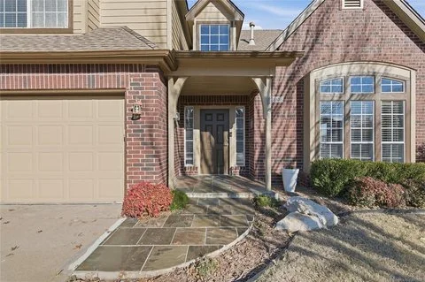 Front entrance of a house with a brick facade, a small porch, and a black front door, flanked by a garage on the left and a large bay window on the right.