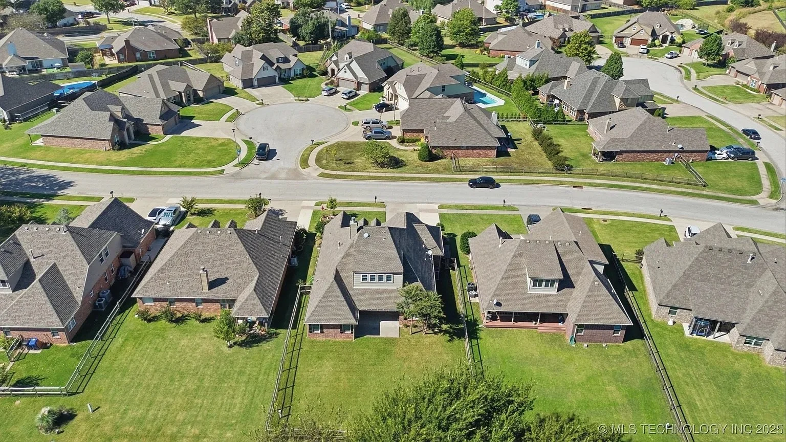 Aerial view of a suburban neighborhood with single-family houses, green lawns, and a curved street with parked cars.