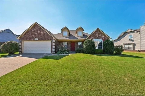 Front view of a single-family house with brick exterior, attached garage, red front door, and well-maintained green lawn.
