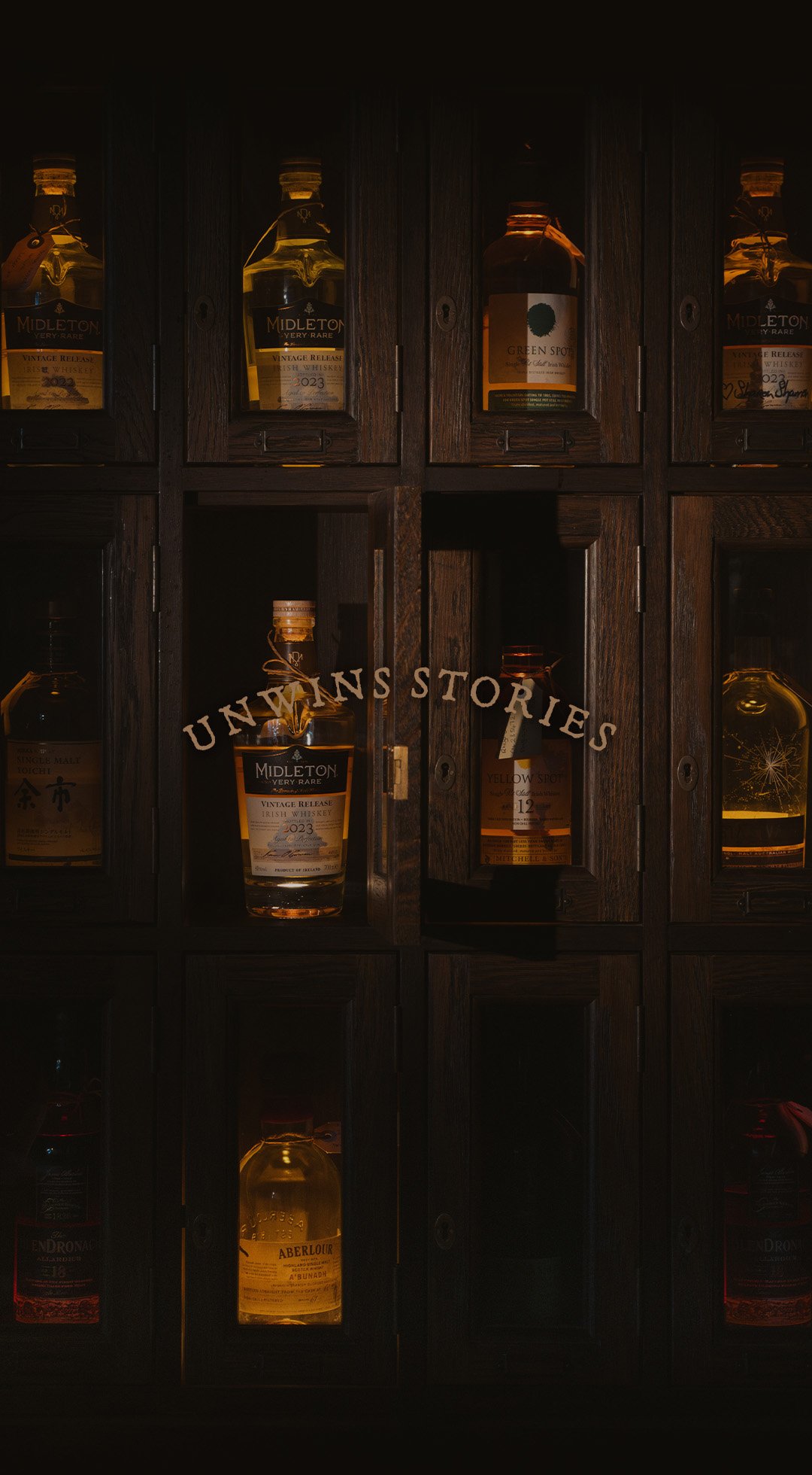 Dark wooden cabinet with shelves containing bottles of whiskey, with the label 'Unwins Stories' on the glass.