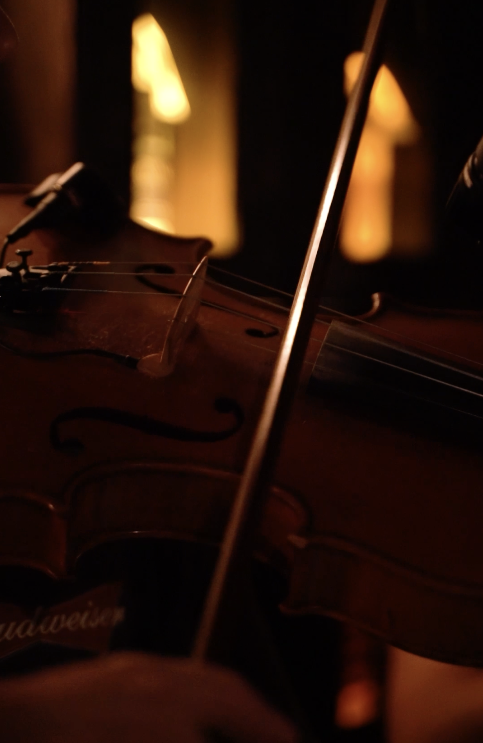 Close-up of a violin with a warm, dimly lit background, showcasing its wooden body and strings.