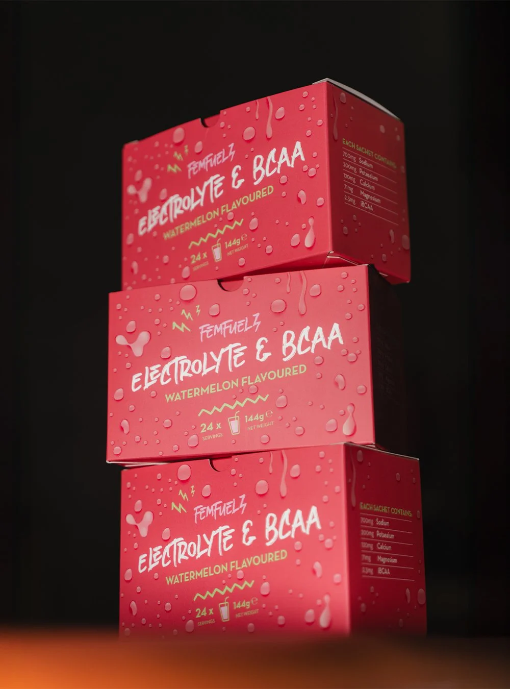 Three stacked boxes of FemFuelz watermelon-flavored electrolyte and BCAA supplement with a pink design, water droplets, and product information on a black background.
