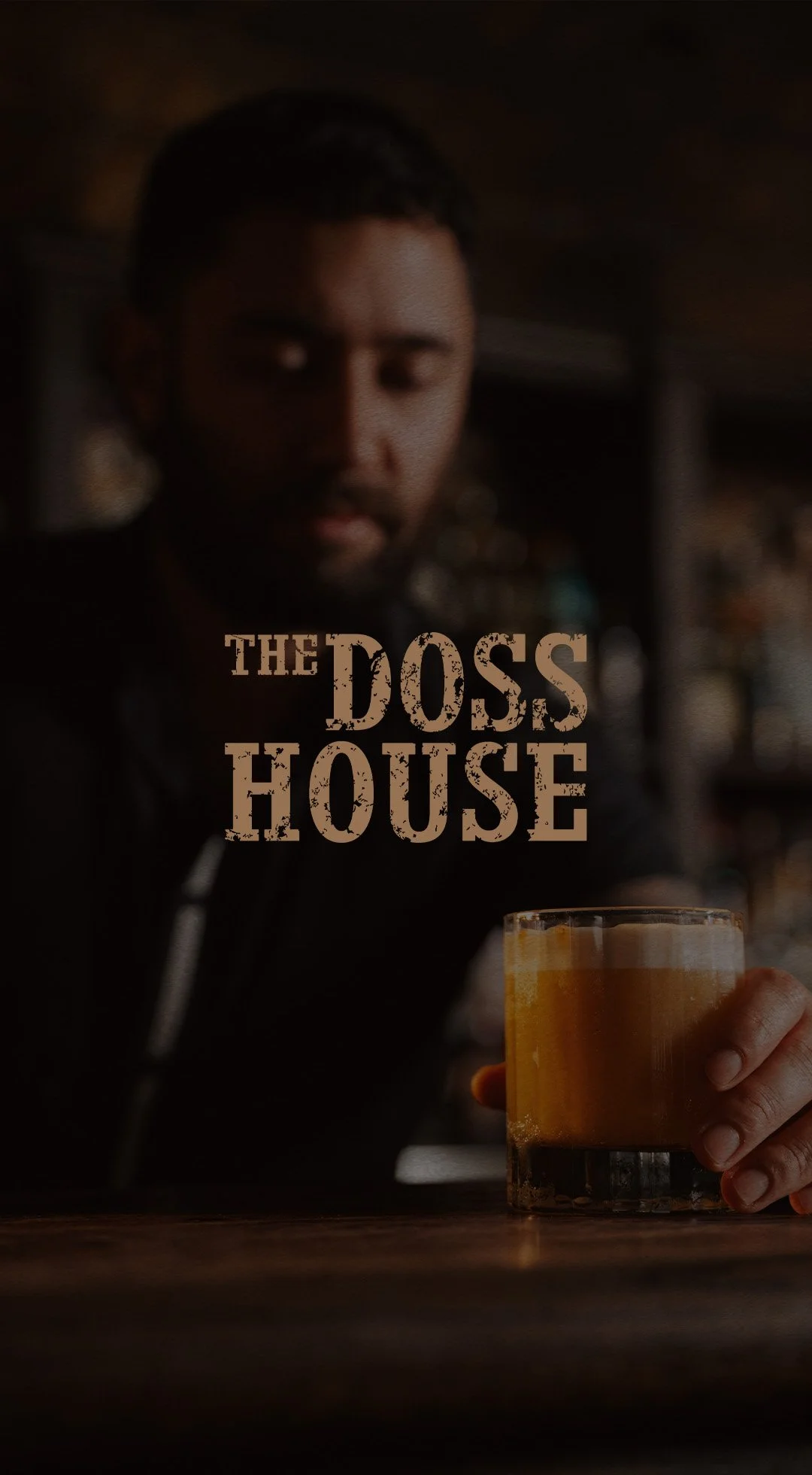 A man holding a glass of beer in a dimly lit bar with the text 'The Doss House' overlayed.