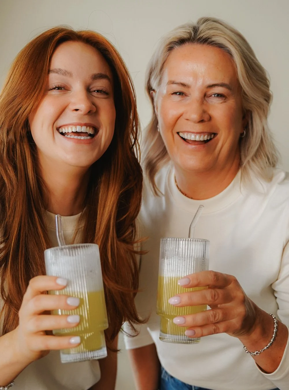 Two women smiling and celebrating with drinks in clear glasses.