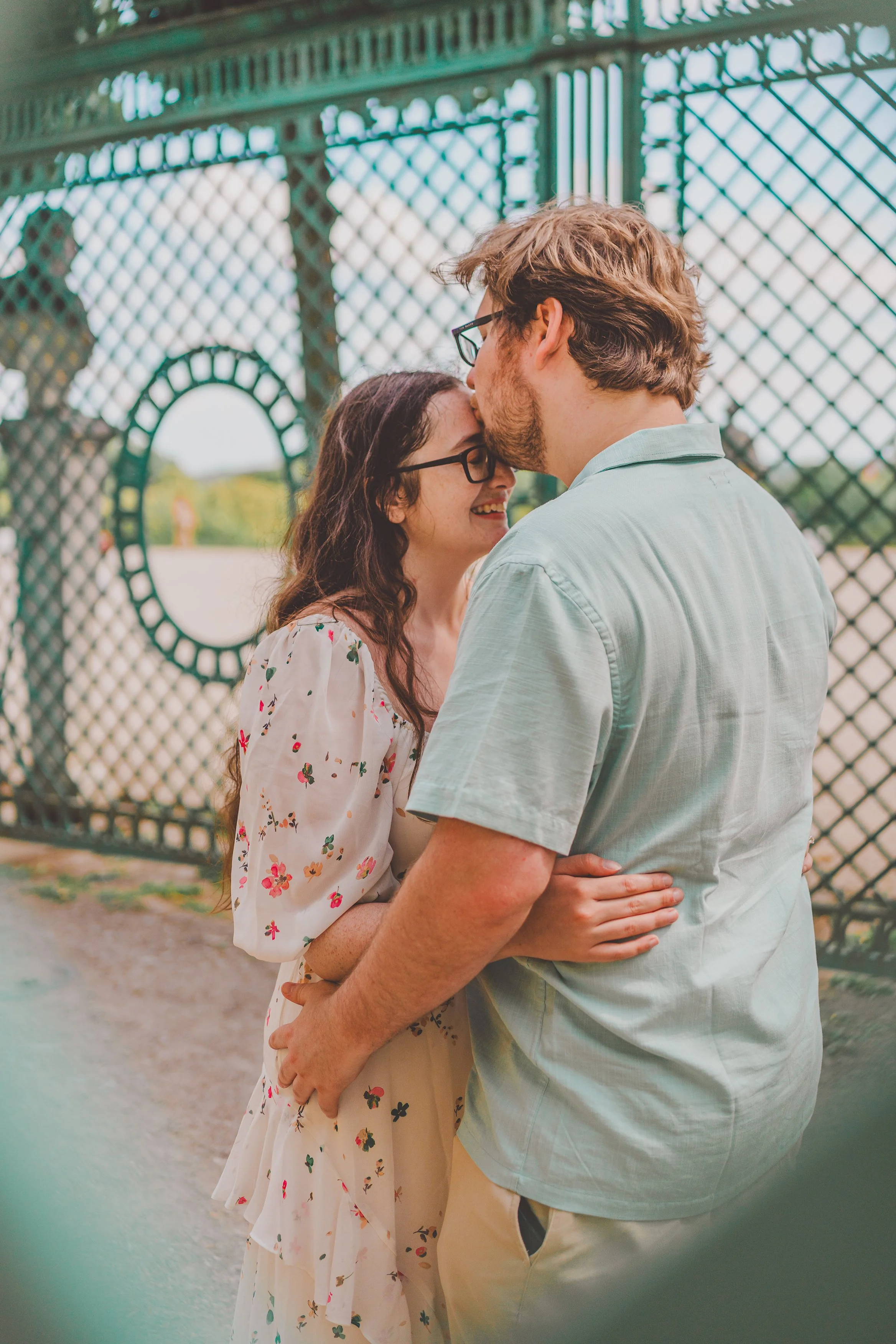 A couple in love sharing a tender moment under a decorative bridge, with the woman smiling and the man leaning in for a kiss.