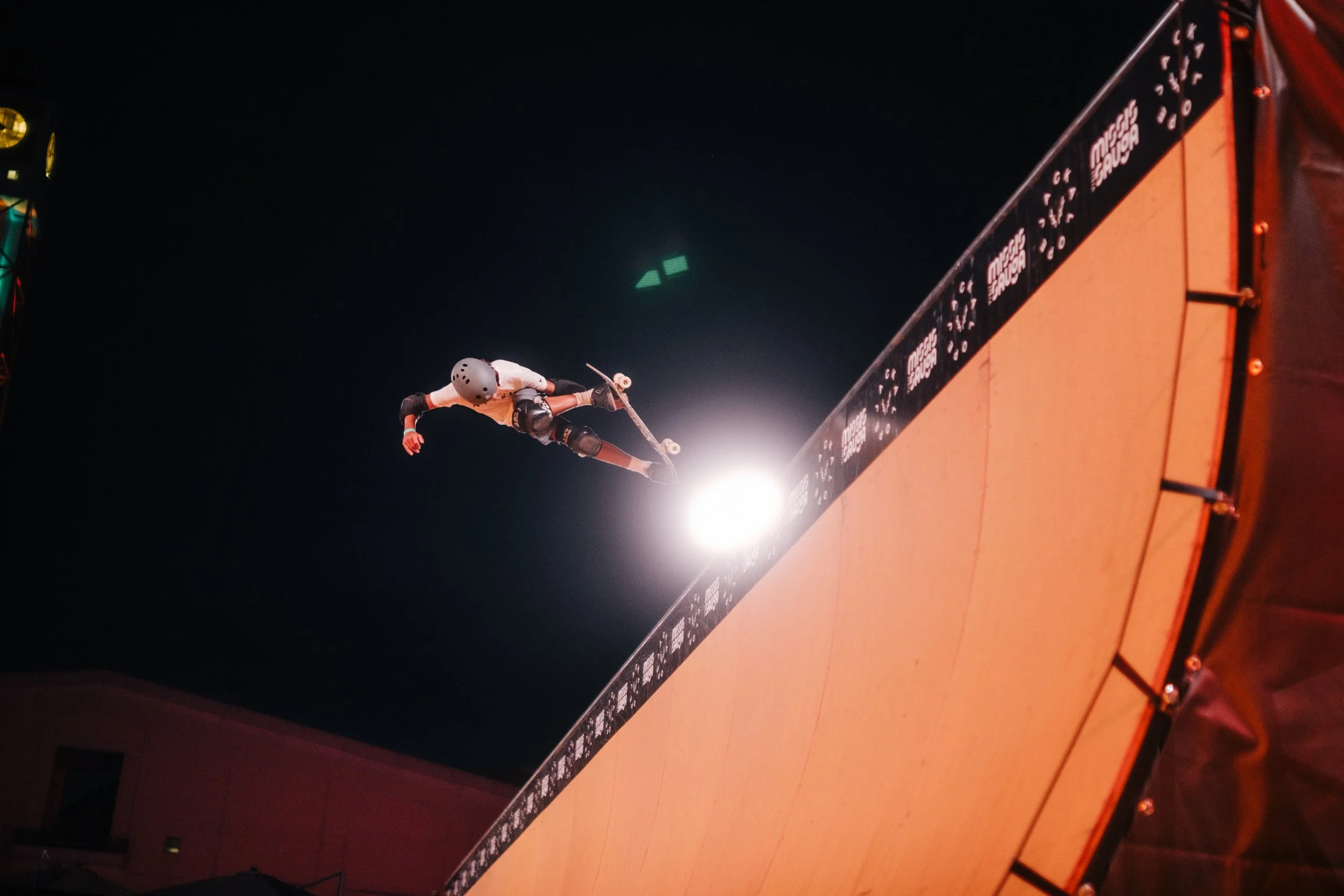 A skateboarder performing a stunt on a ramp at night, illuminated by bright lights.