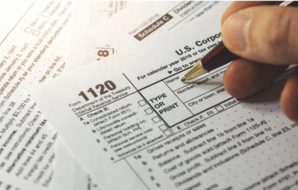Close-up of a person filling out a U.S. Treasury Department tax form 1120 with a black and gold pen.