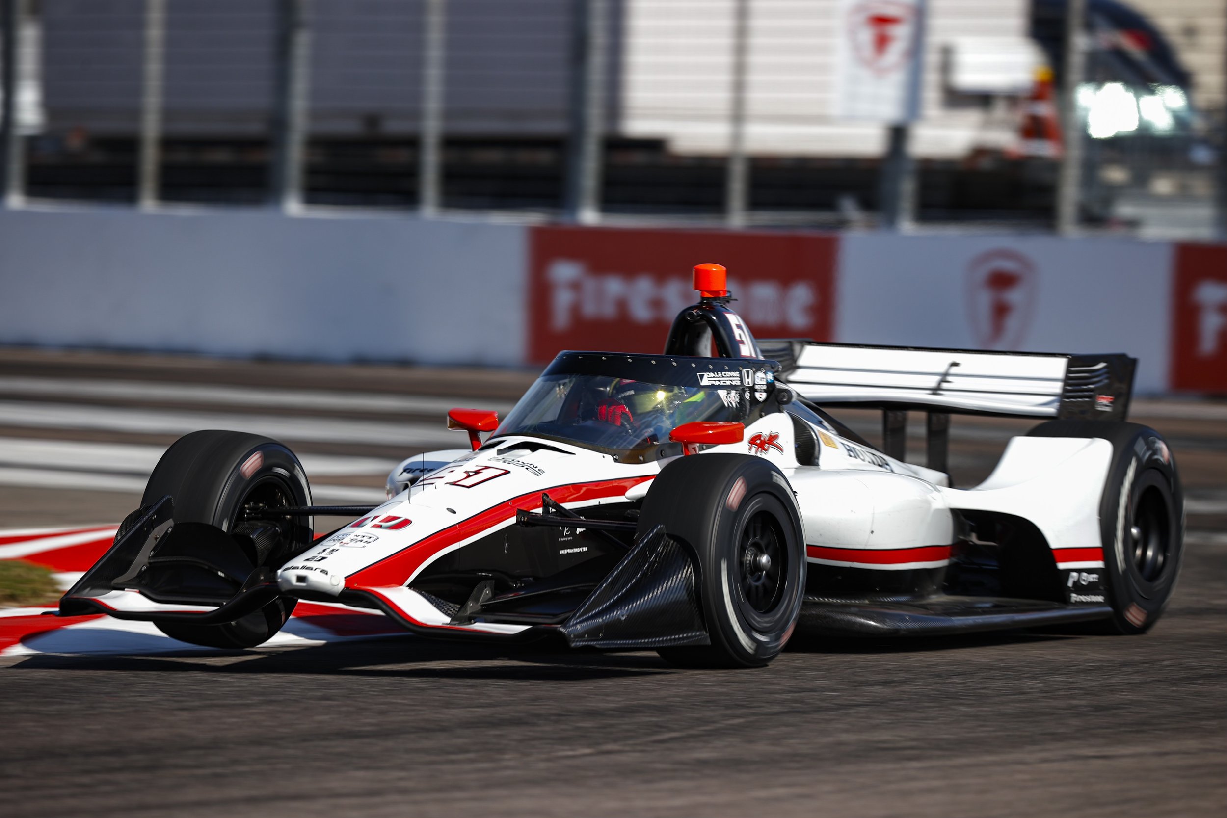 A race car with a white body, red and black accents, and a large rear wing, speeding on a race track.
