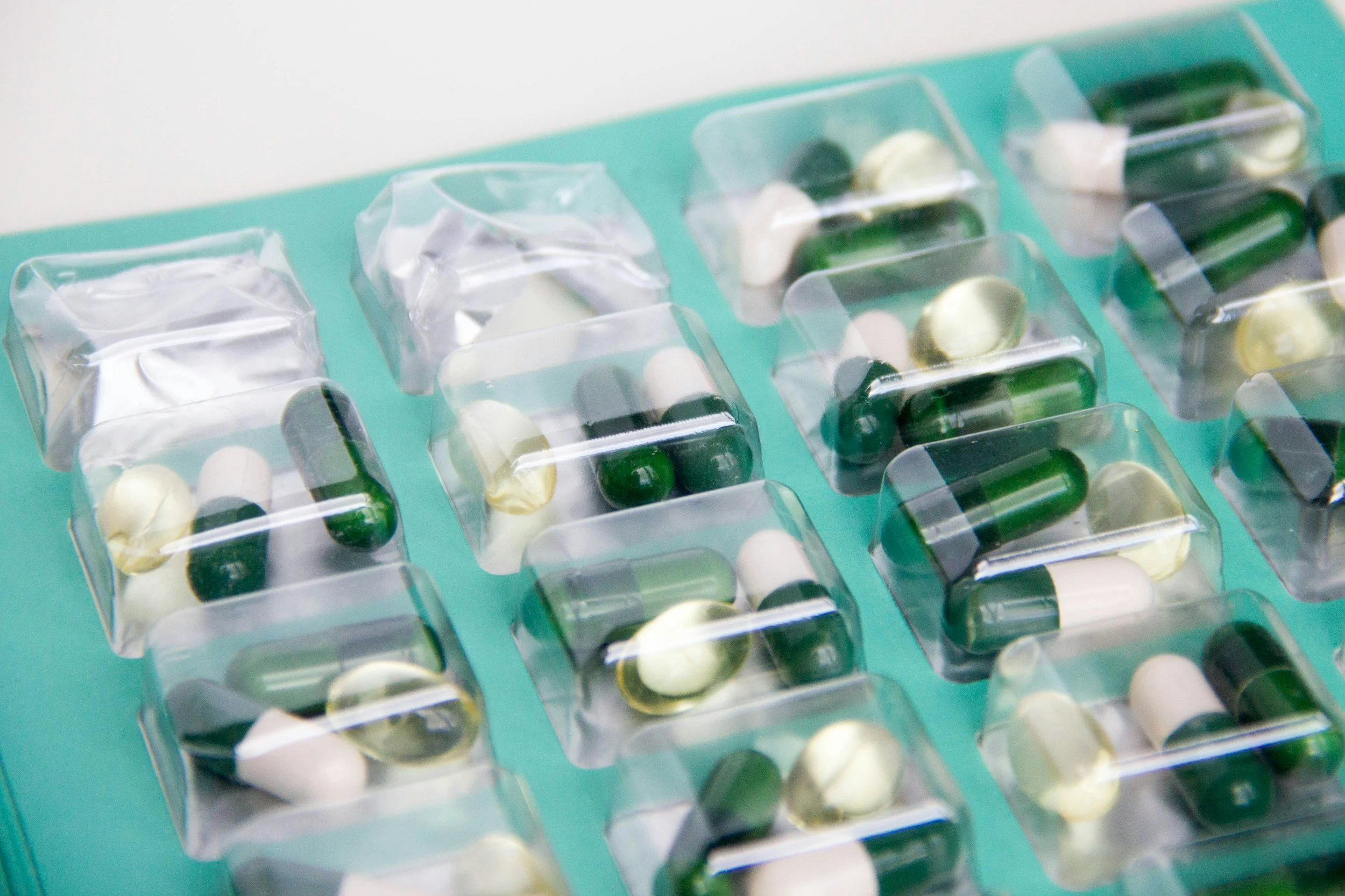 Close-up of blister packs containing green and white capsules on a teal background.