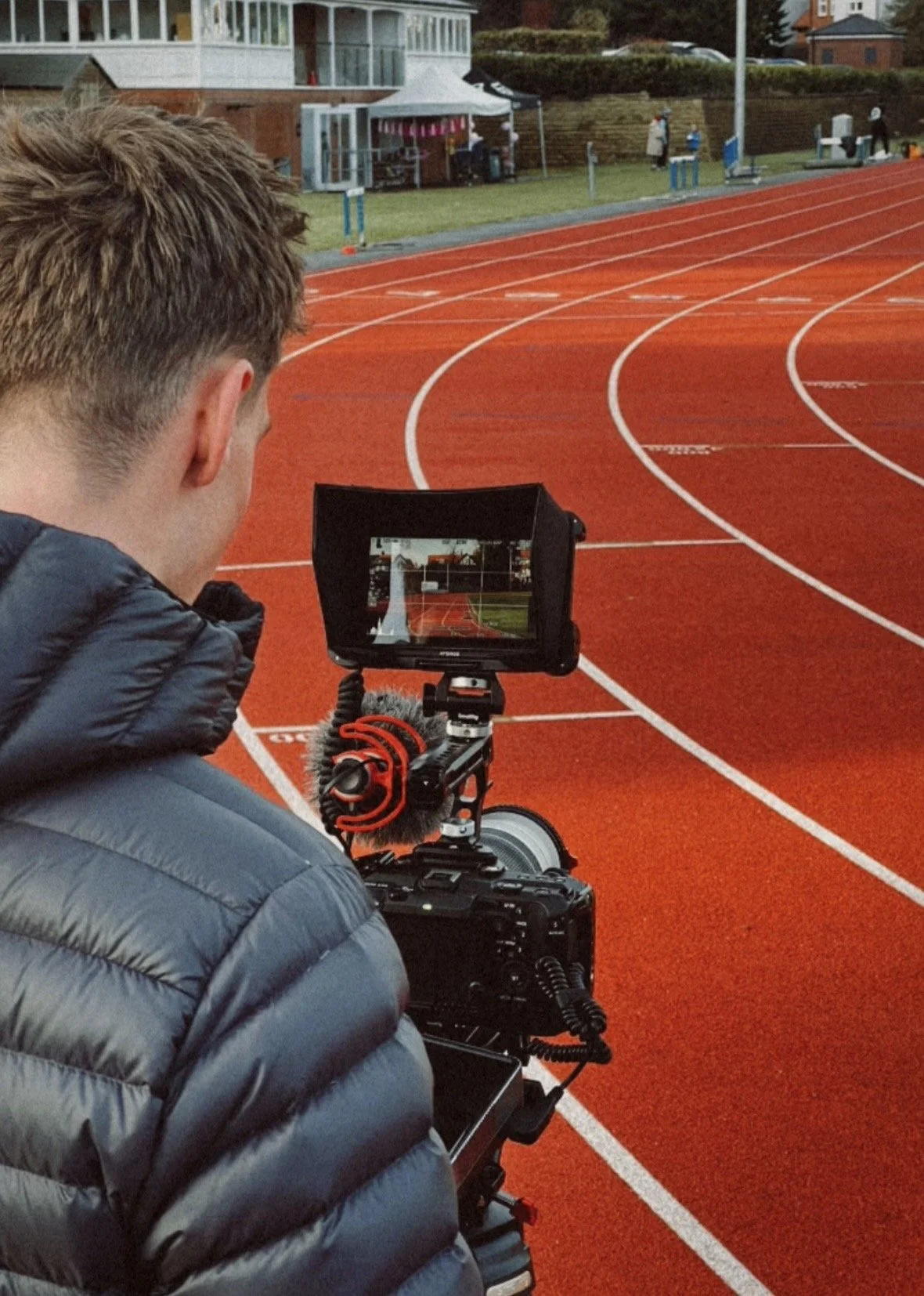 A person takes photographs on a red running track with a camera mounted on a tripod, capturing the field and stadium.