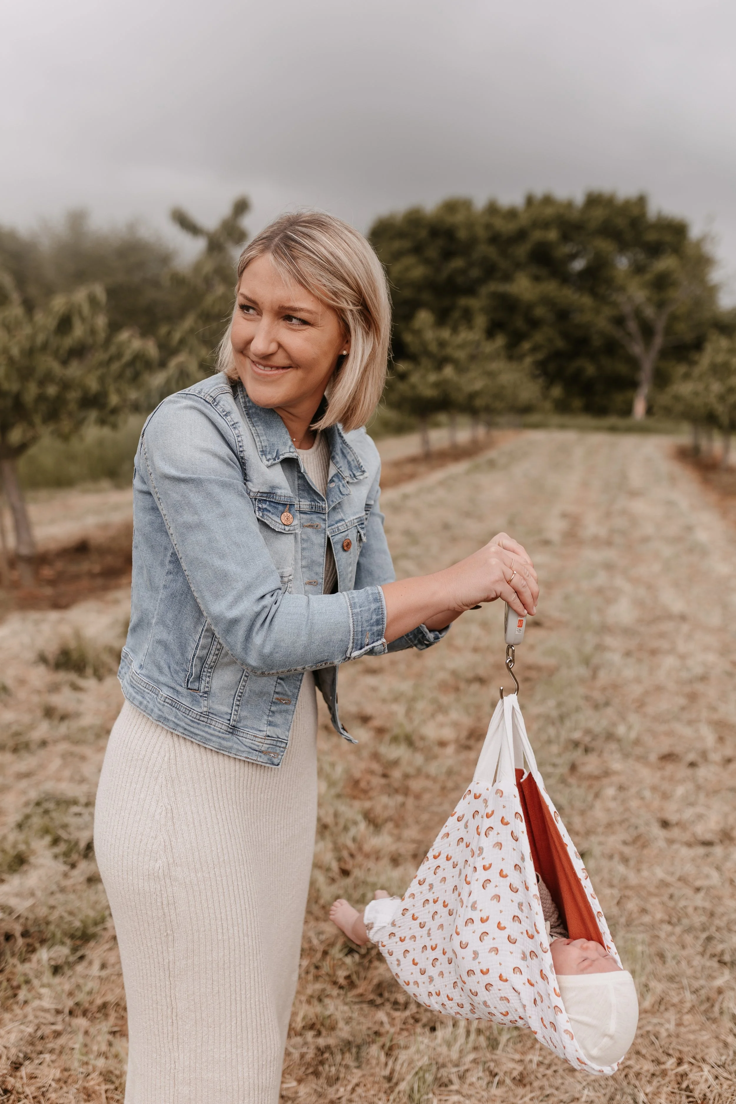 Eine Frau hält einen tragbaren Autositz mit einem schlafenden Baby in einem Blumenfeld.