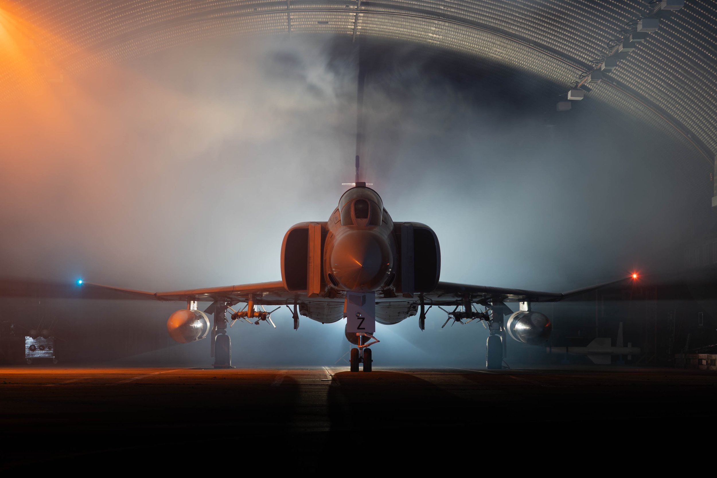 A McDonnell Douglas F-4 parked inside a Hardened Aircraft Shelter with smoke, illuminated by soft lighting.