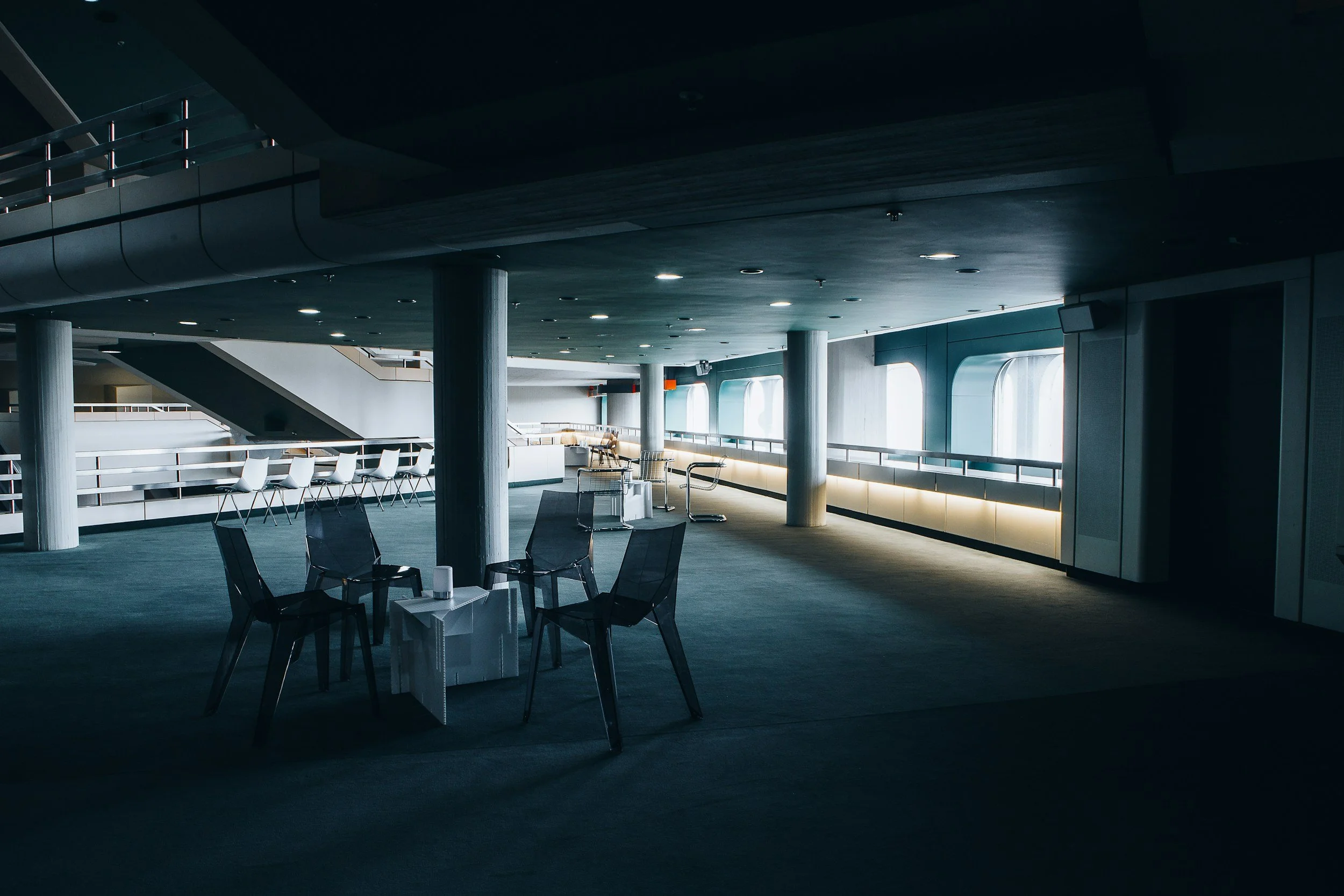 Empty modern airport lounge with chairs, tables, and large windows letting in natural light.