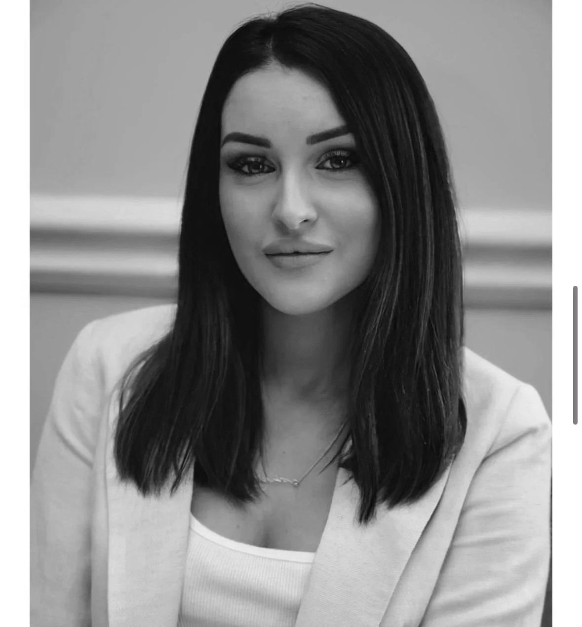 Black and white portrait of a woman with straight, shoulder-length dark hair, wearing a light-colored blazer and a necklace.