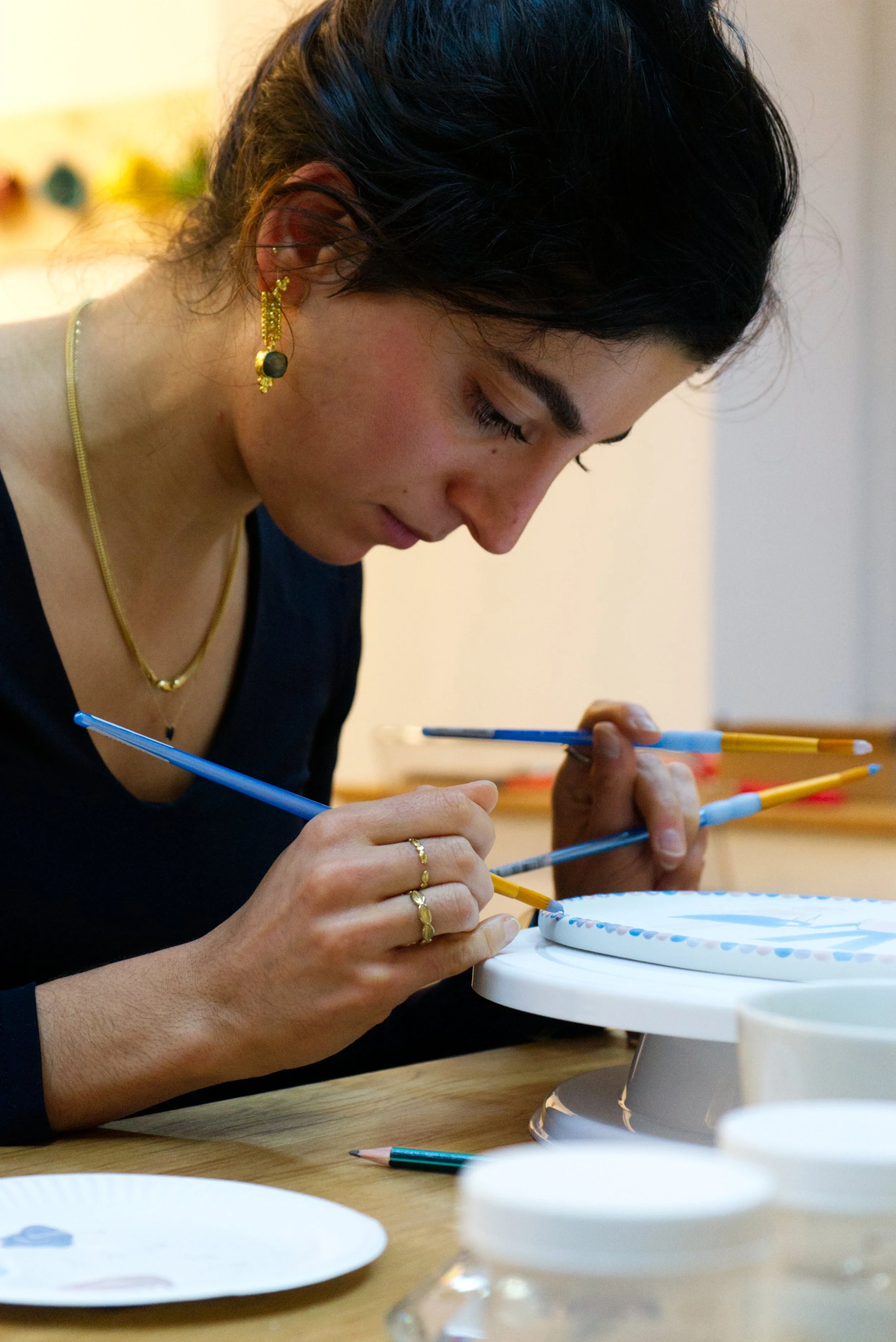 Eine Frau dekoriert einen weißen Teller mit blauer Musterung mit einem Pinsel.