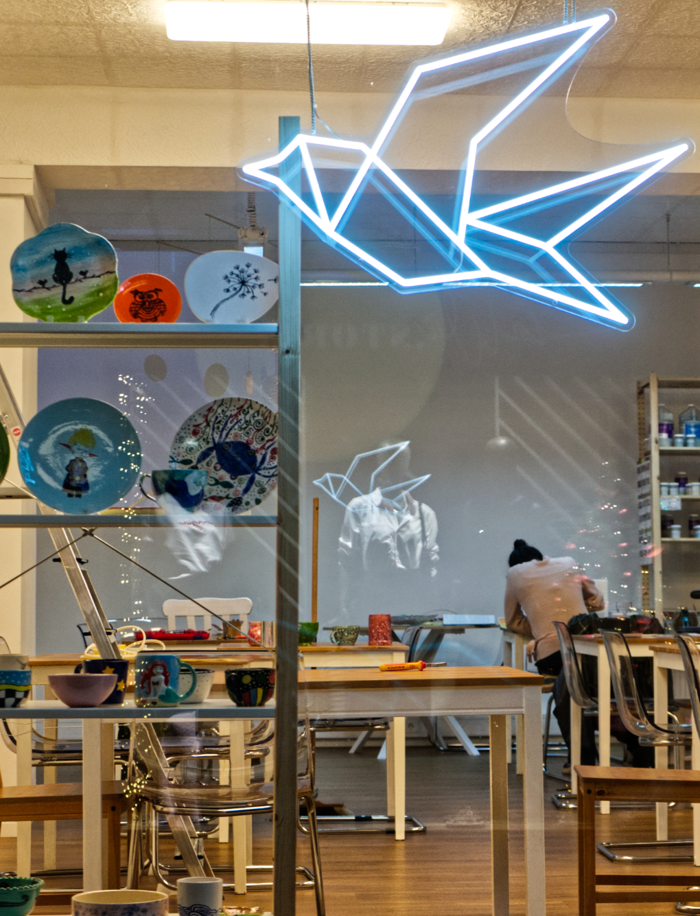 Ein Blick in einen Laden, der handgemachte Keramik- und Porzellanartikel verkauft, mit einer Neon-Schwanüberschrift und einer Person, die am Tisch arbeitet.