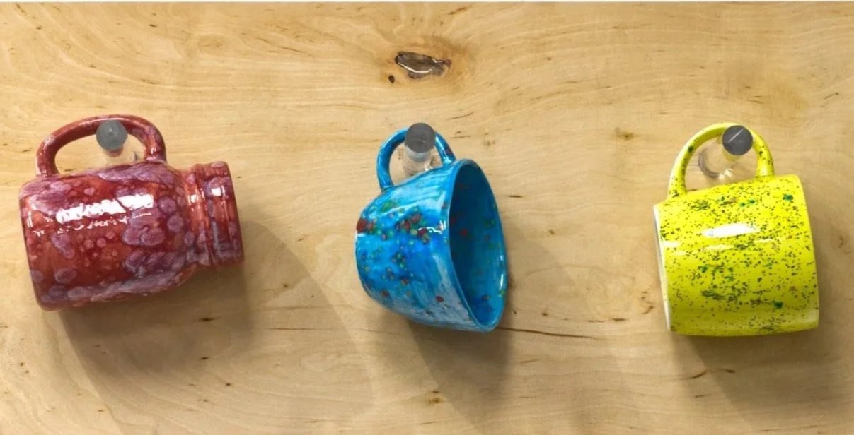 Drei bunt bemalte Tassen, die an einem Holzbrett befestigt sind.