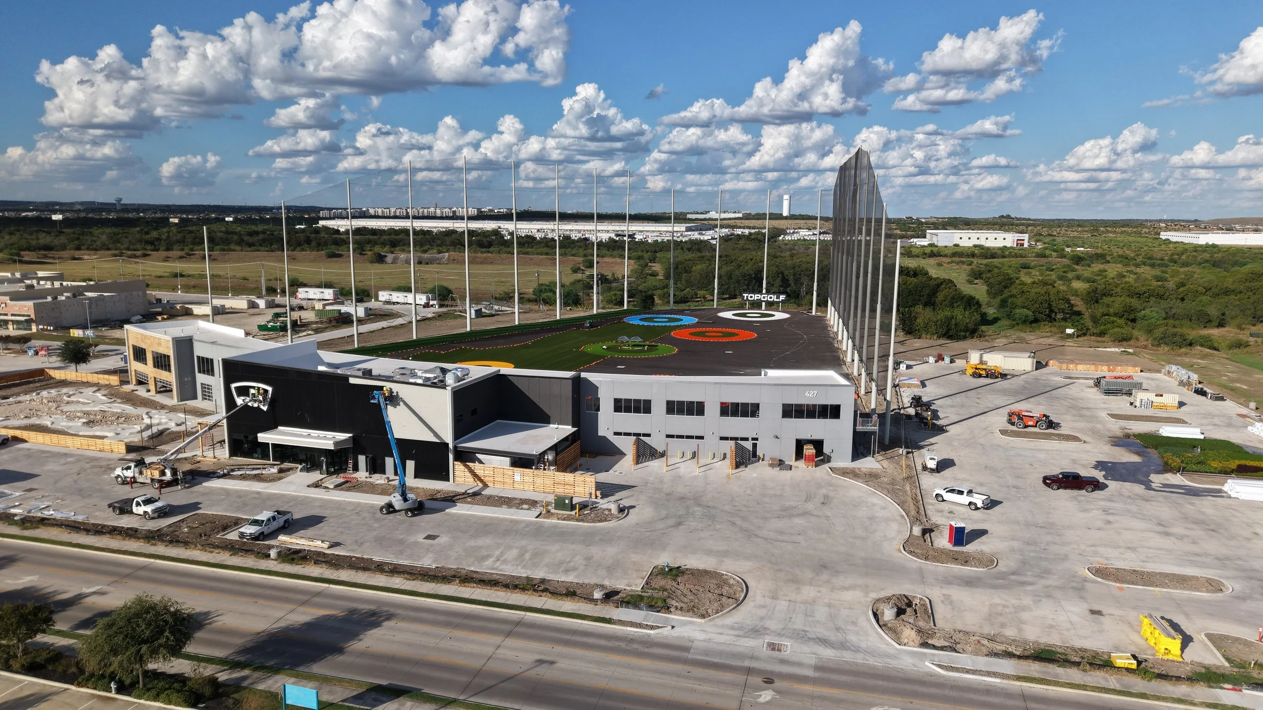 Construction site with a building featuring a racing-themed logo, a mini golf course, and tall poles in the background under a partly cloudy sky.
