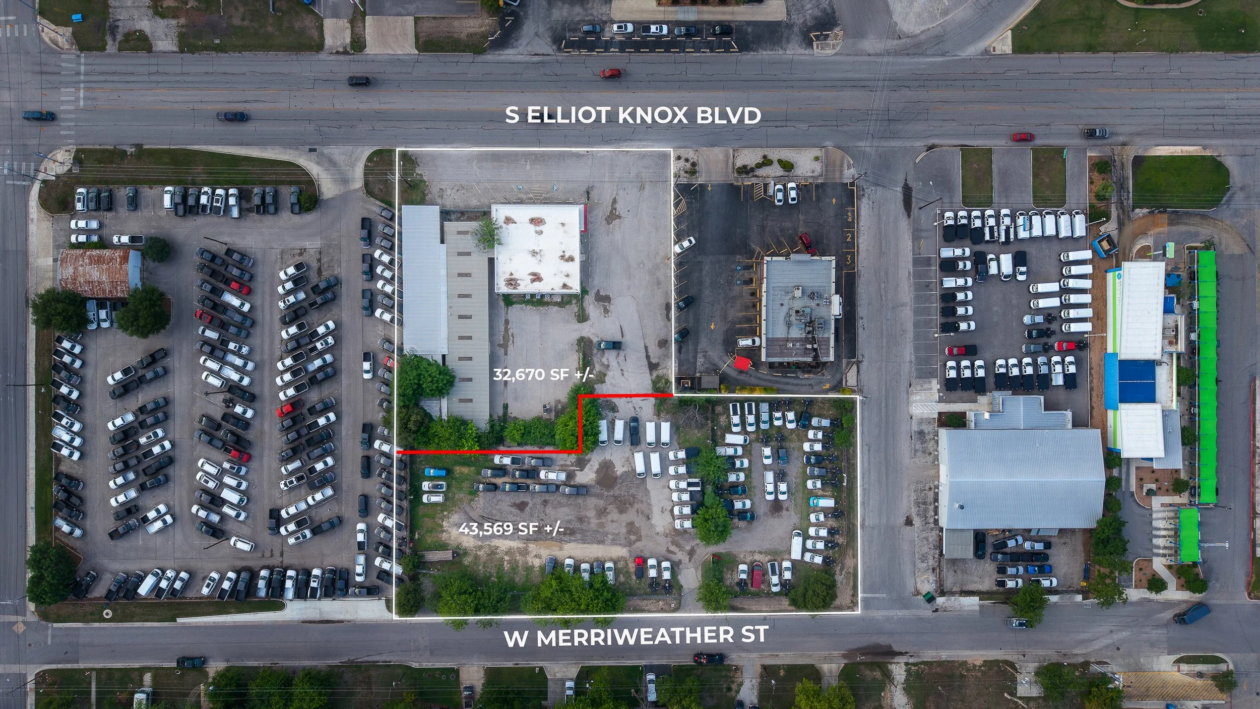 An aerial view of a parking lot located between W Merriweather Street at the bottom and S Elliot Knox Boulevard at the top. The parking lot contains numerous white, black, and gray vehicles, with some marked for designated parking spaces. There are two outlined areas within the parking lot, one measuring approximately 32,670 square feet and another about 43,569 square feet, with the latter in the lower part of the lot. Surrounding the parking lot are buildings, some trees, and adjacent streets.