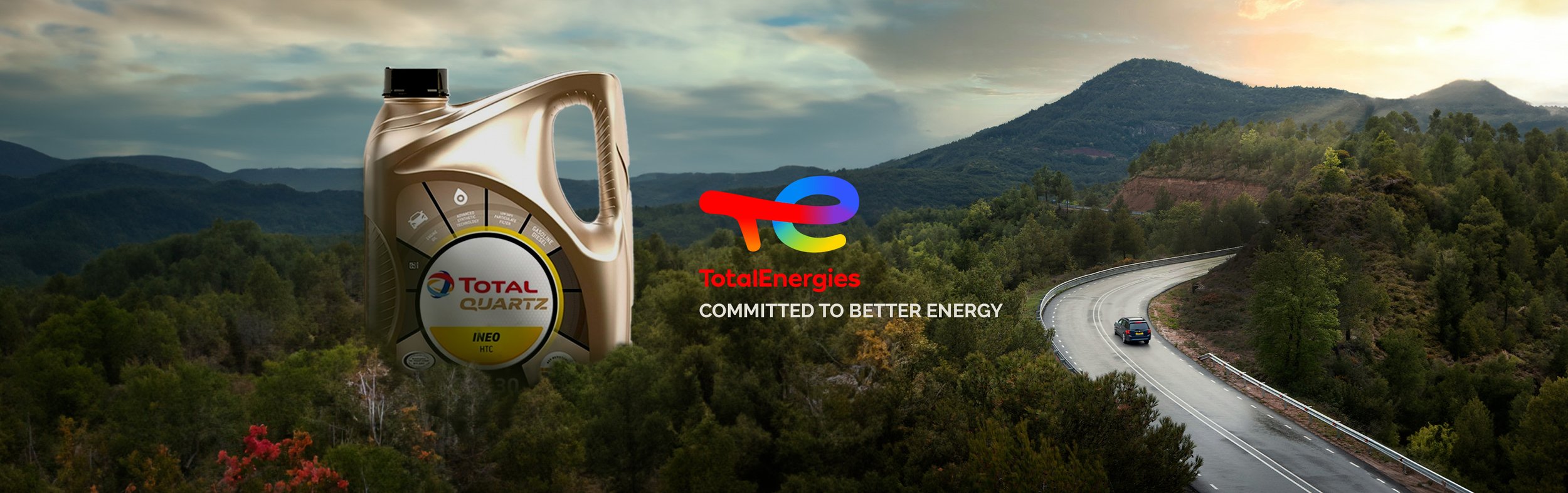 A large bottle of Total Quartz motor oil in front of a scenic landscape with mountains, a winding road, and trees, with the TotalEnergies logo and the slogan 'Committed to Better Energy' visible.