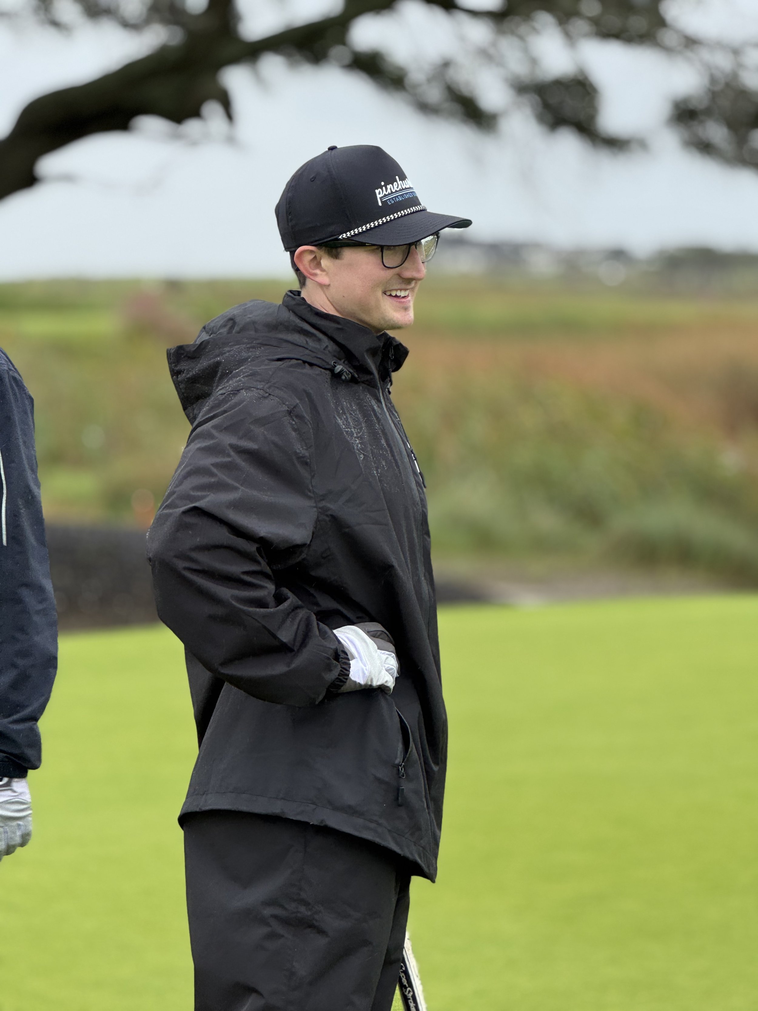 A man in golf attire, smiling while holding a putter on the green